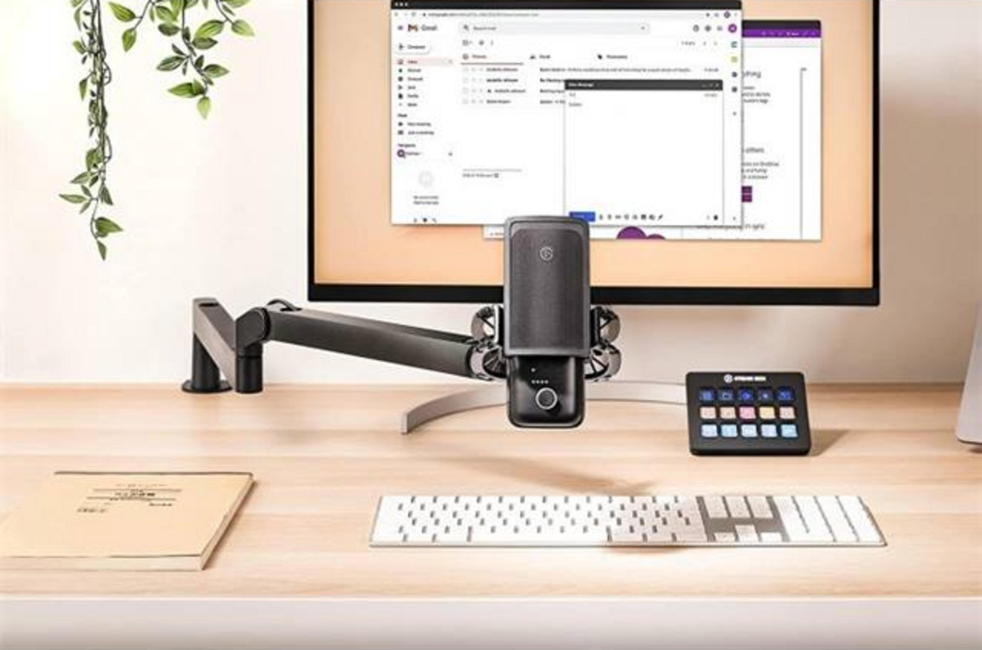 Biurko z monitorem, mikrofonem, klawiaturą i notatnikiem.