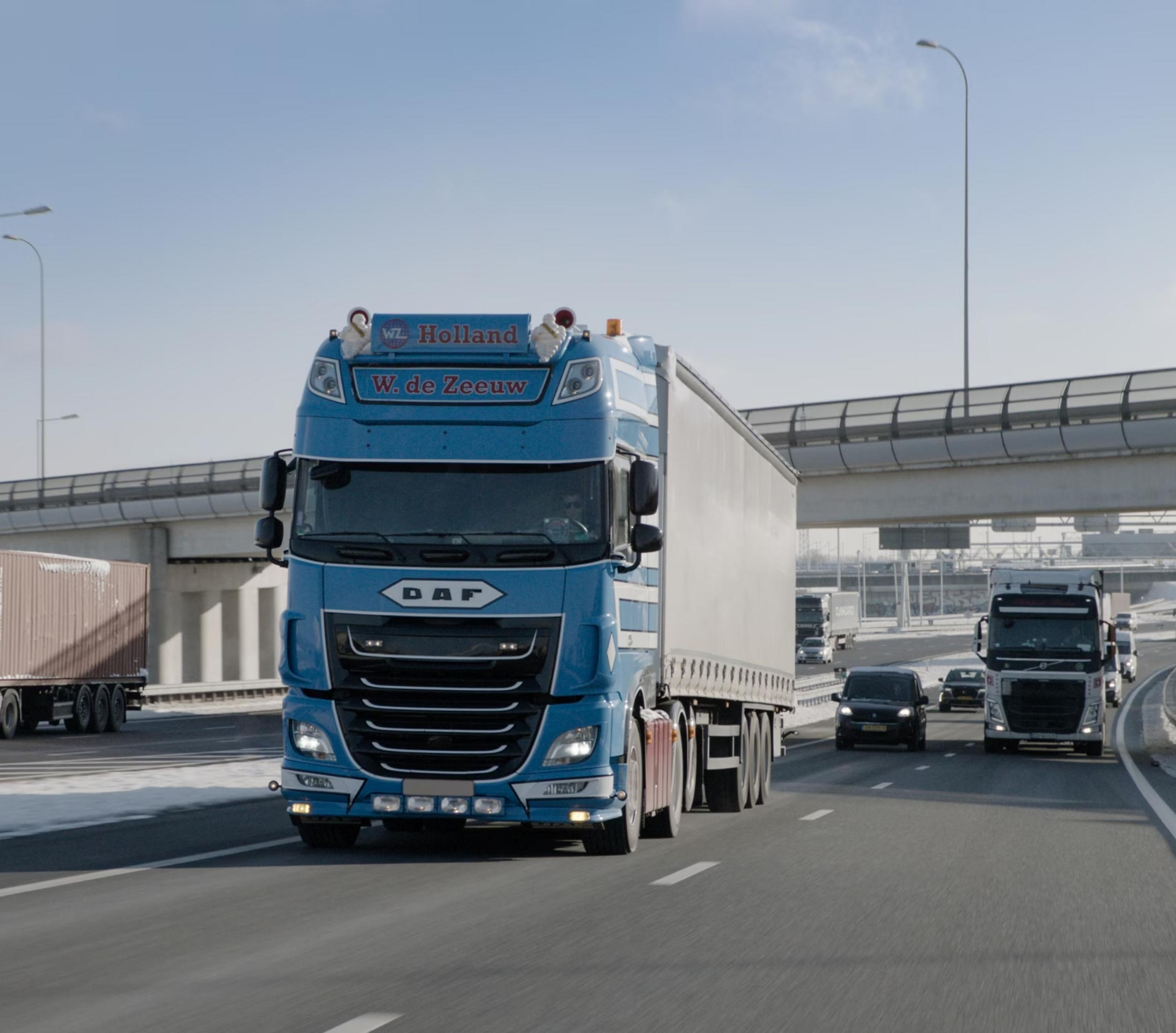 Blauer LKW mit Anhänger fährt auf Autobahn, Schnee am Straßenrand.