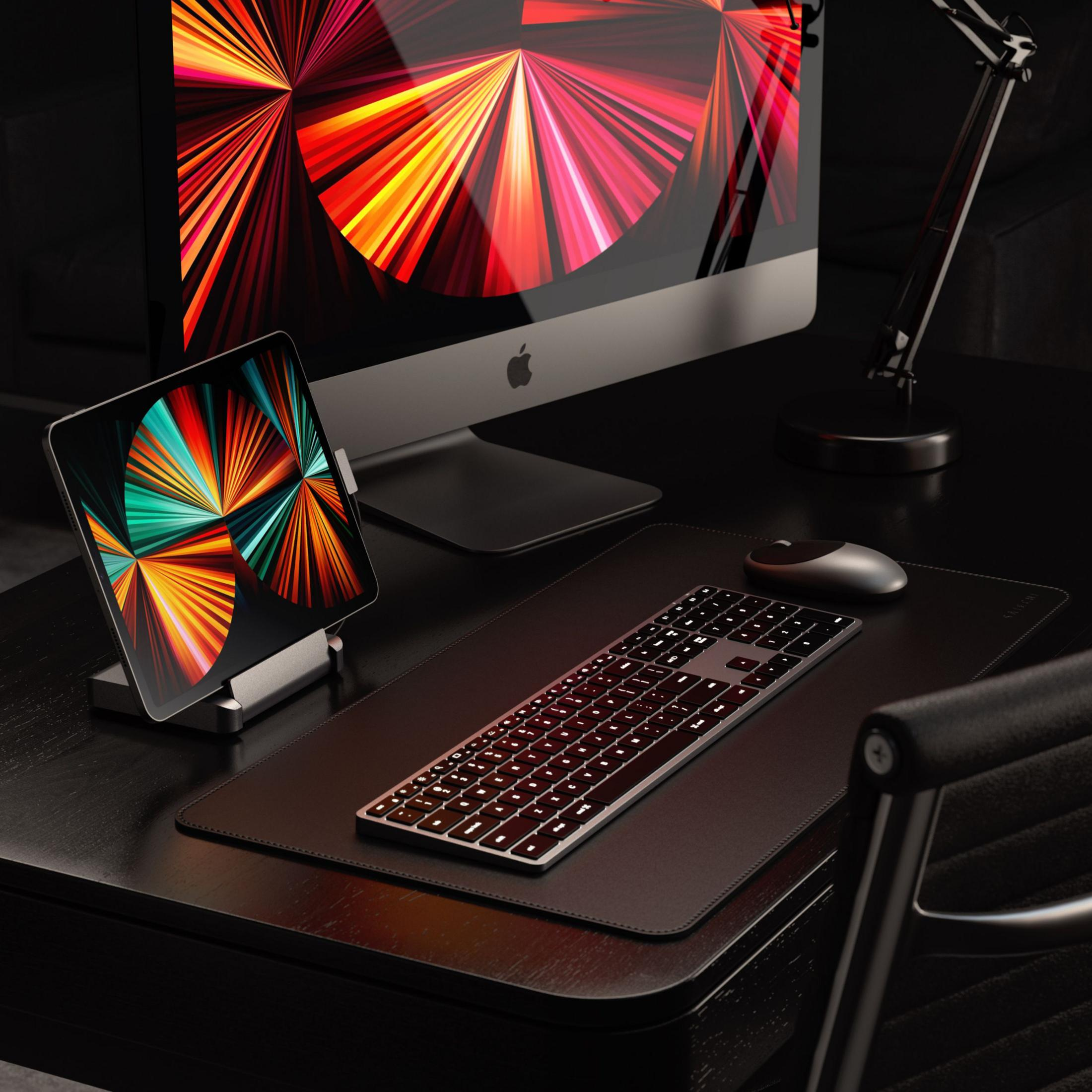 Ein Schreibtisch mit iMac, Tablet, Tastatur und Maus. Bunte Tapete.