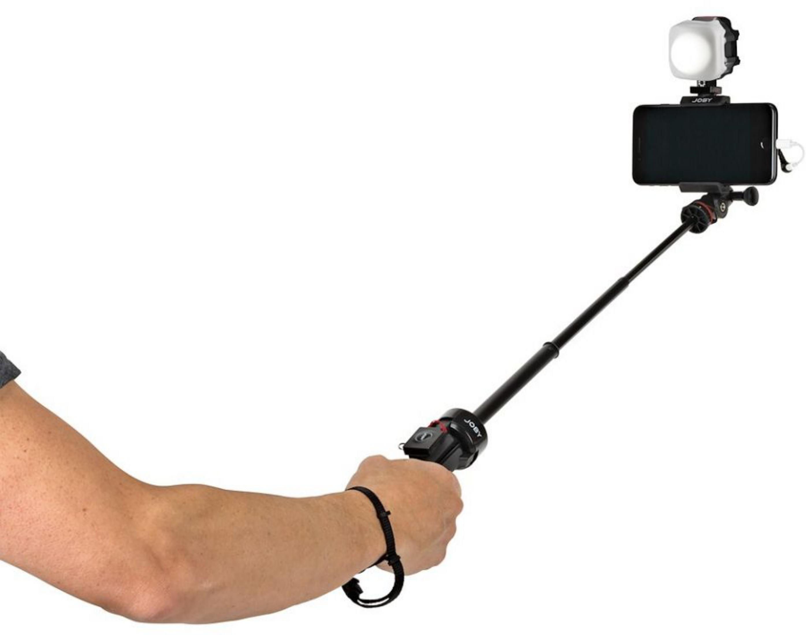 Ein Arm hält einen schwarzen Selfie-Stick mit Smartphone und Licht auf weißem Hintergrund.
