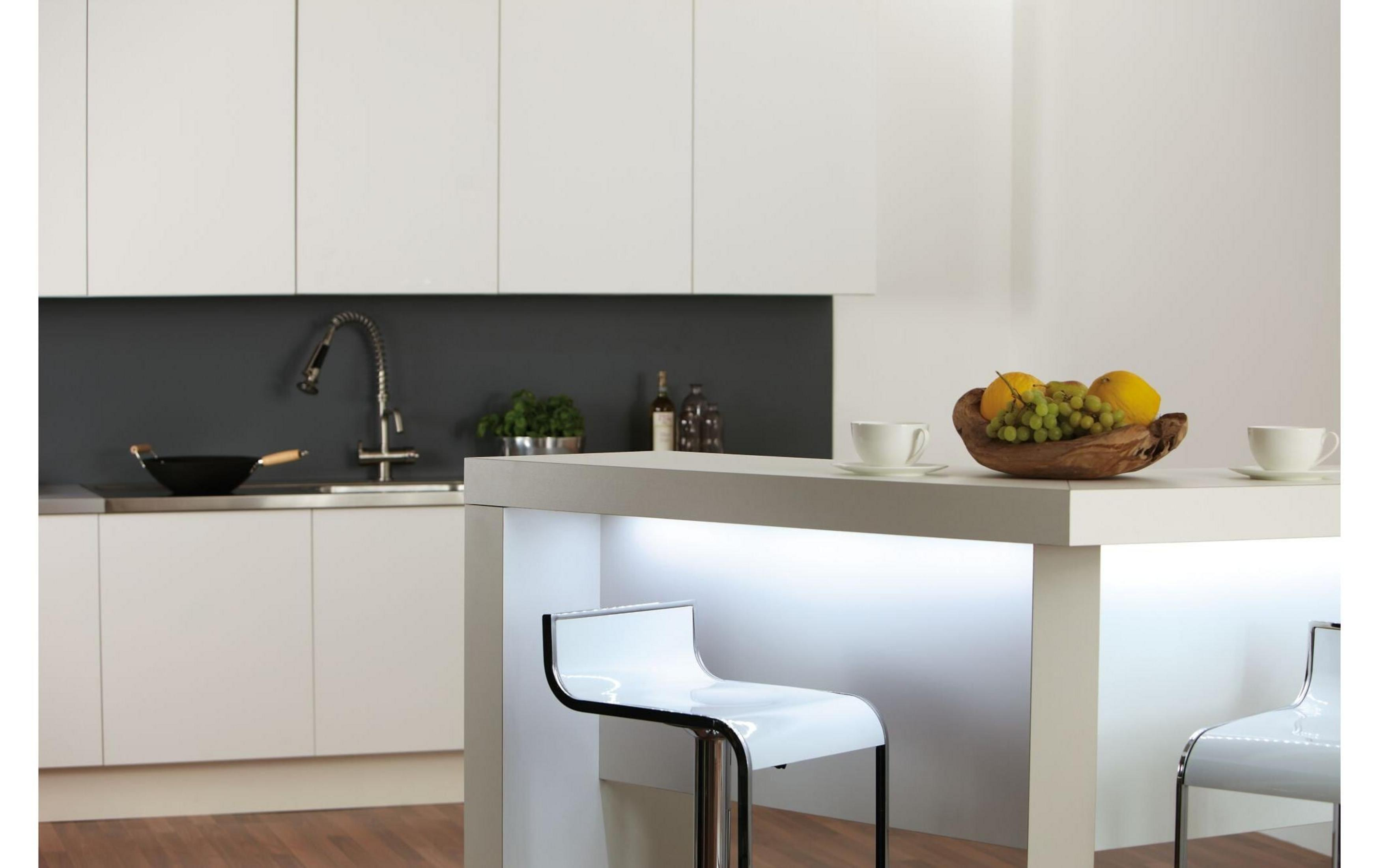 Nowoczesna kuchnia z białym blatem, barem i misą owoców.