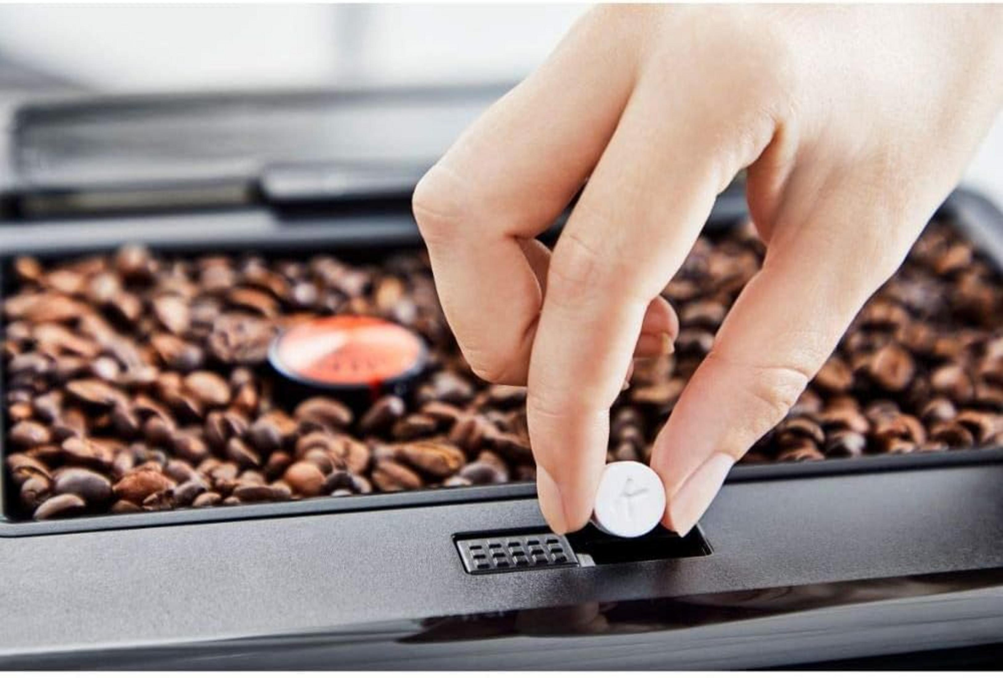 Una mano pone una compressa bianca in una macchina da caffè con chicchi.