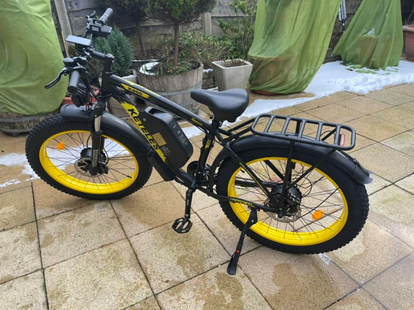 Bicicleta eléctrica negra con llantas amarillas y portaequipajes.
