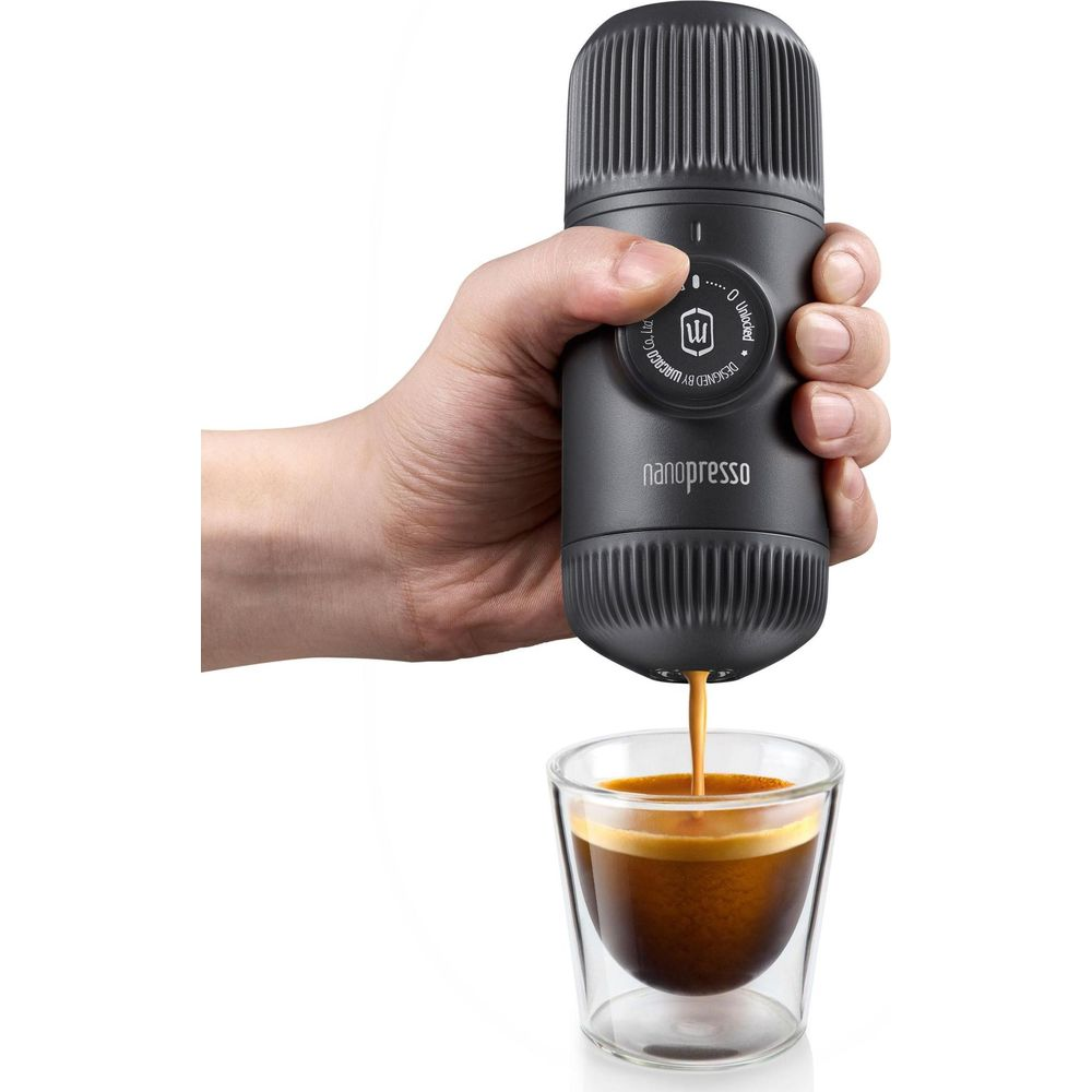 Ręka trzyma czarną maszynę do kawy Nanopresso, dozującą espresso do szklanki.