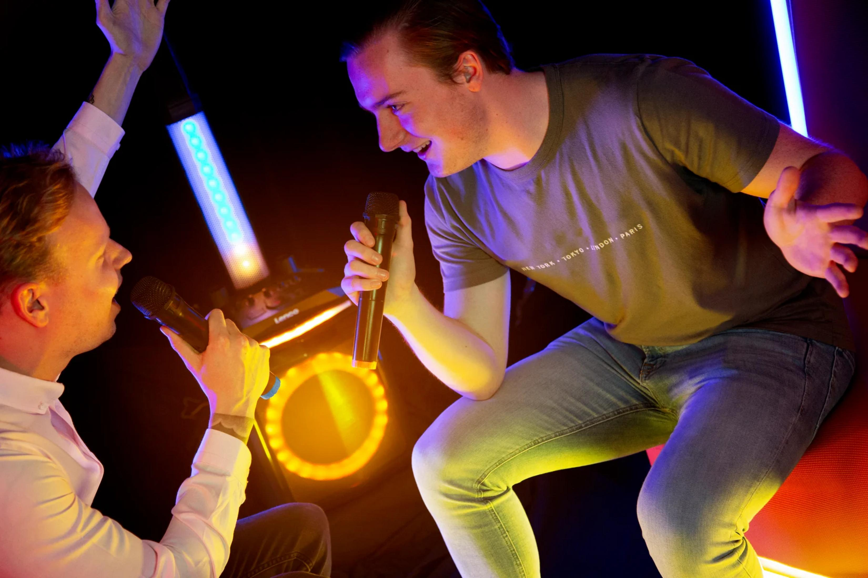 Dwóch mężczyzn śpiewa do mikrofonów na imprezie karaoke z kolorowymi światłami.