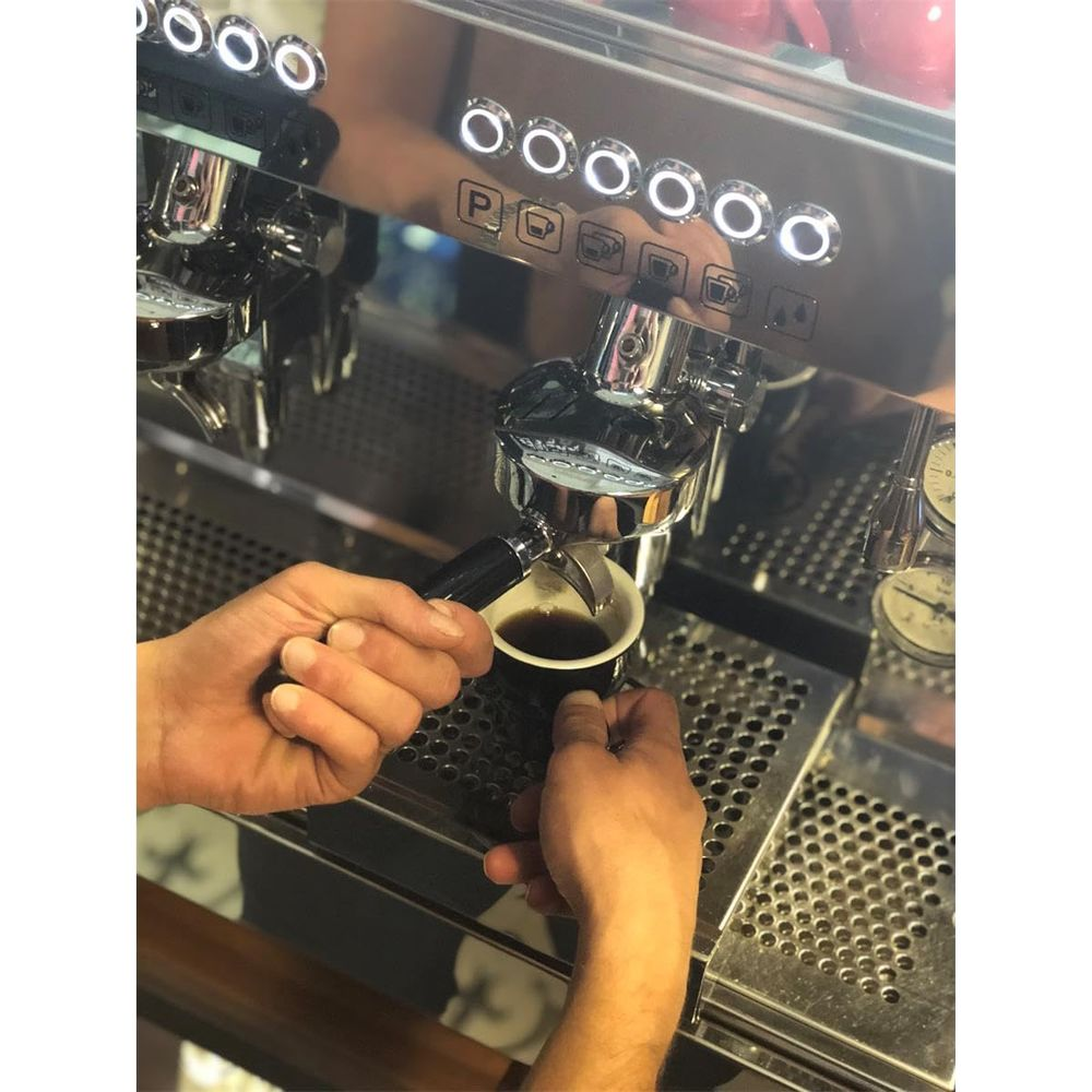 Hände halten eine Espressomaschine, um Kaffee in eine Tasse zu brühen.