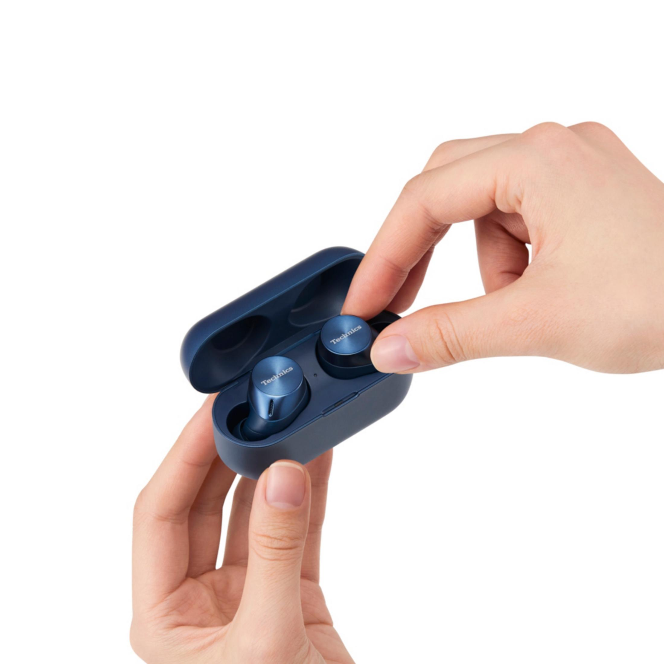 Eine Hand nimmt einen blauen Kopfhörer aus einer blauen Ladebox.