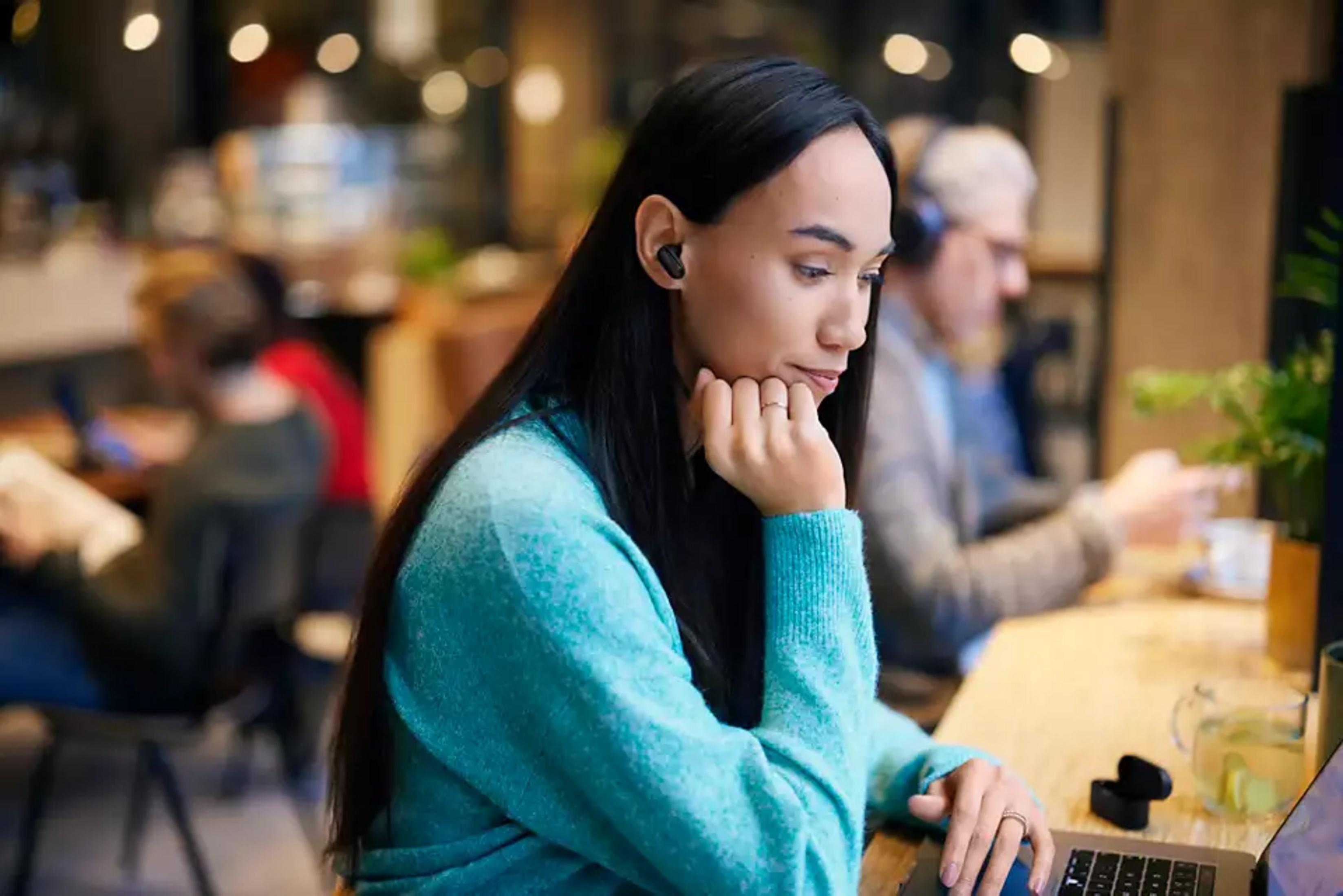 Una mujer con auriculares se sienta en un portátil en un café.