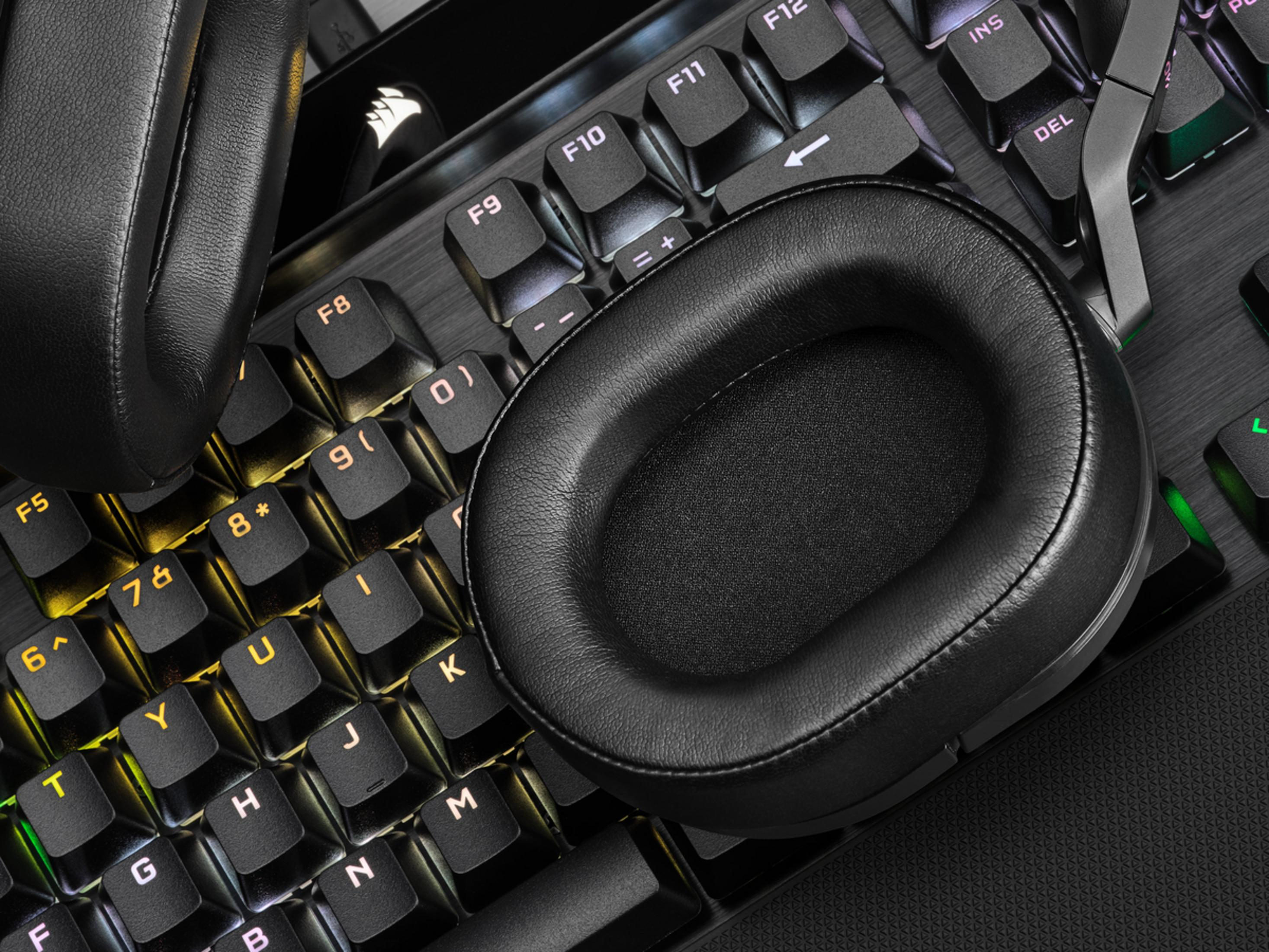 Schwarze Lederkopfhörer liegen auf einer schwarzen mechanischen Tastatur mit gelber und weißer Hintergrundbeleuchtung.