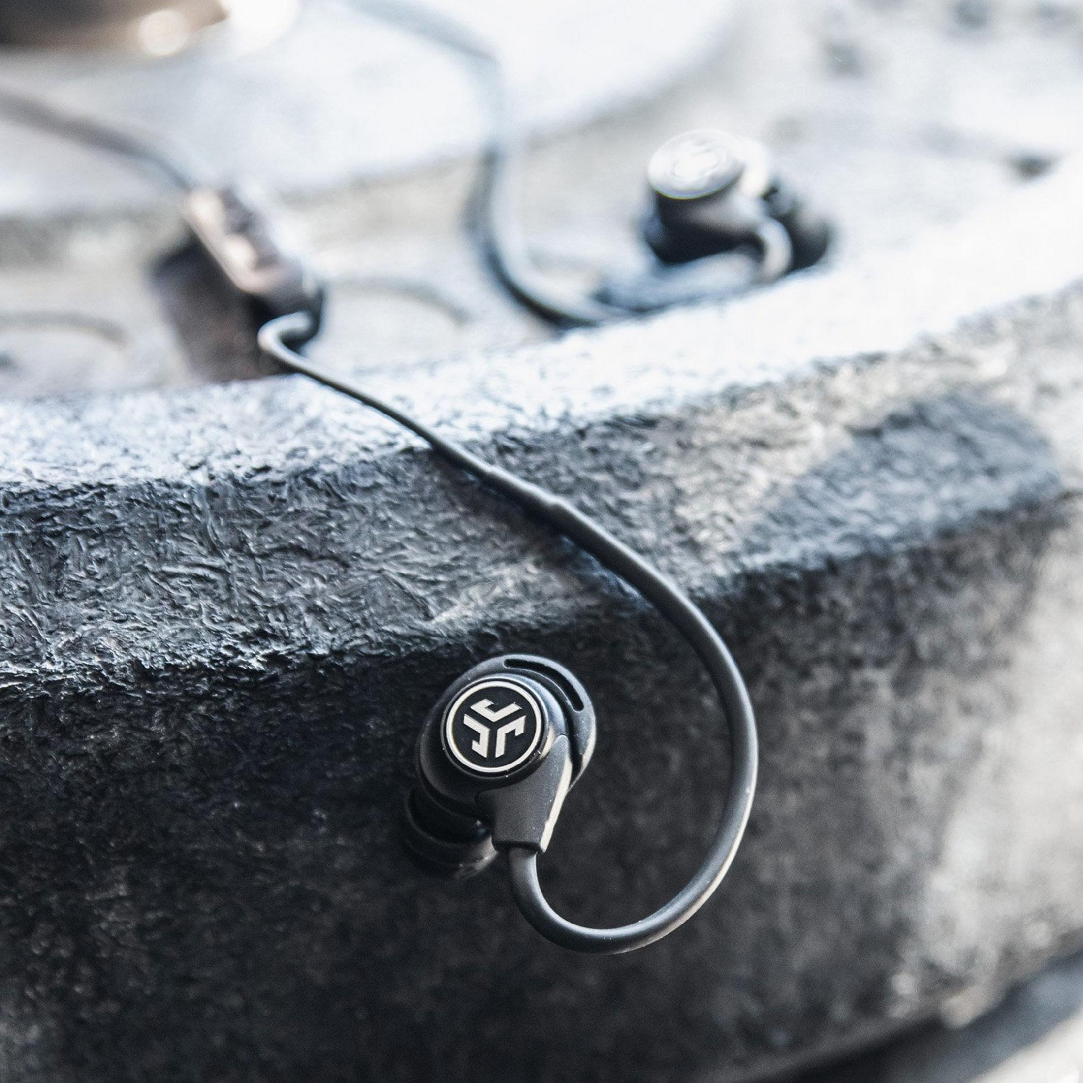 Czarne słuchawki douszne z logo na teksturowanej szarej powierzchni.