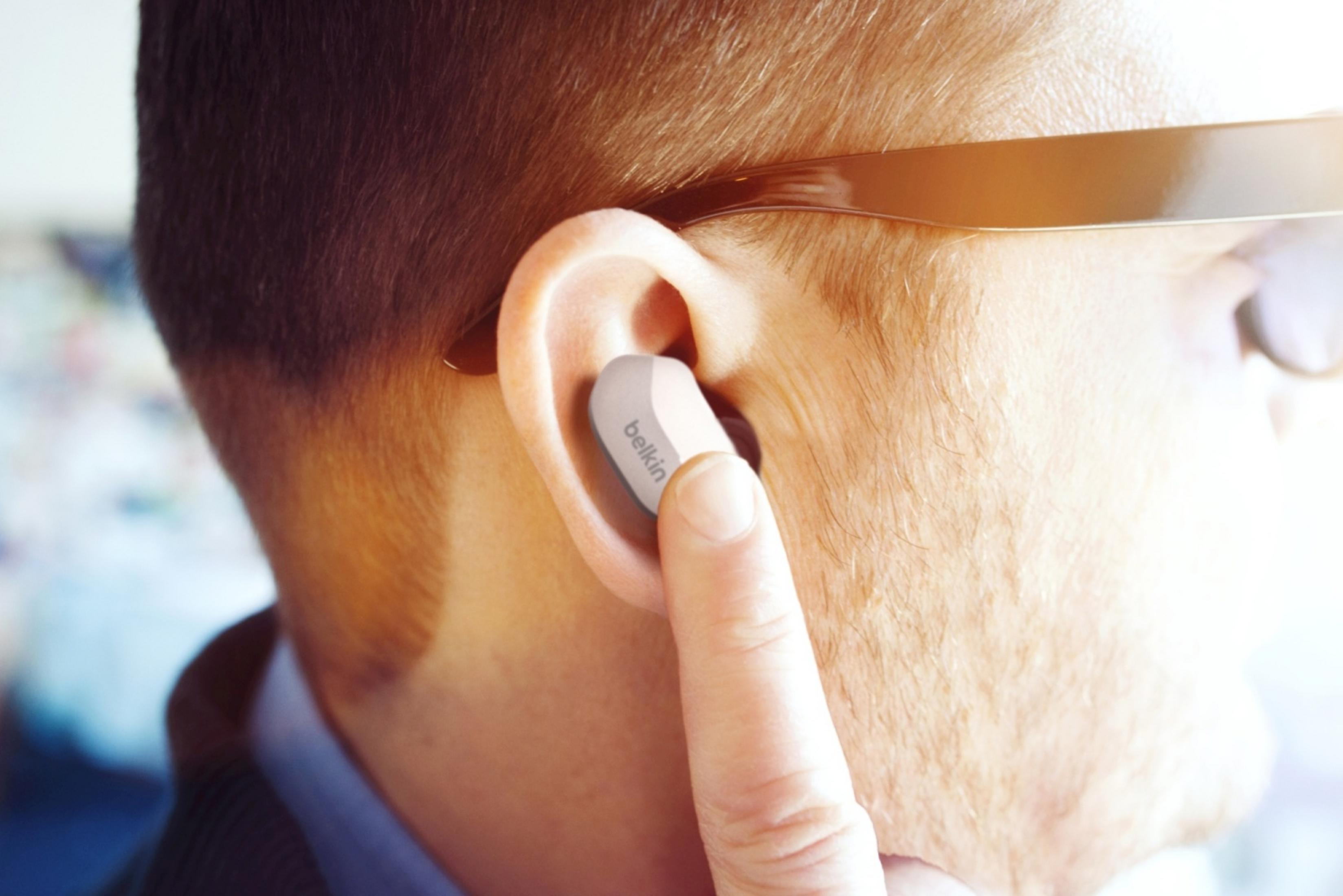 Una persona si inserisce un auricolare Belkin bianco nell'orecchio.