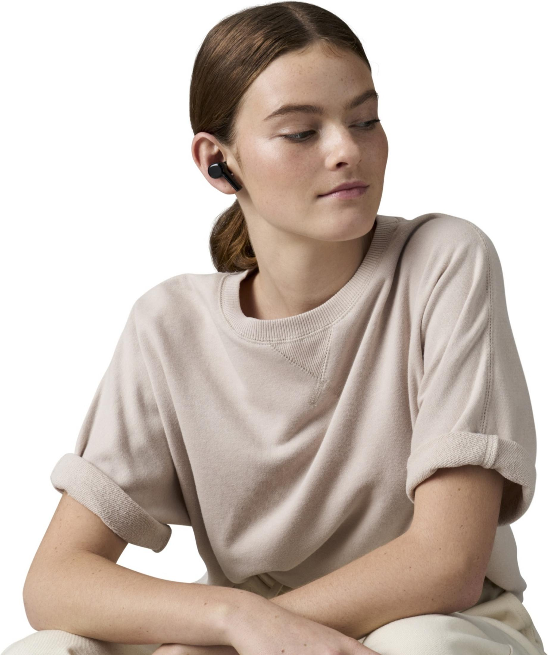 Mujer joven con auriculares negros en la oreja izquierda, lleva sudadera beige.