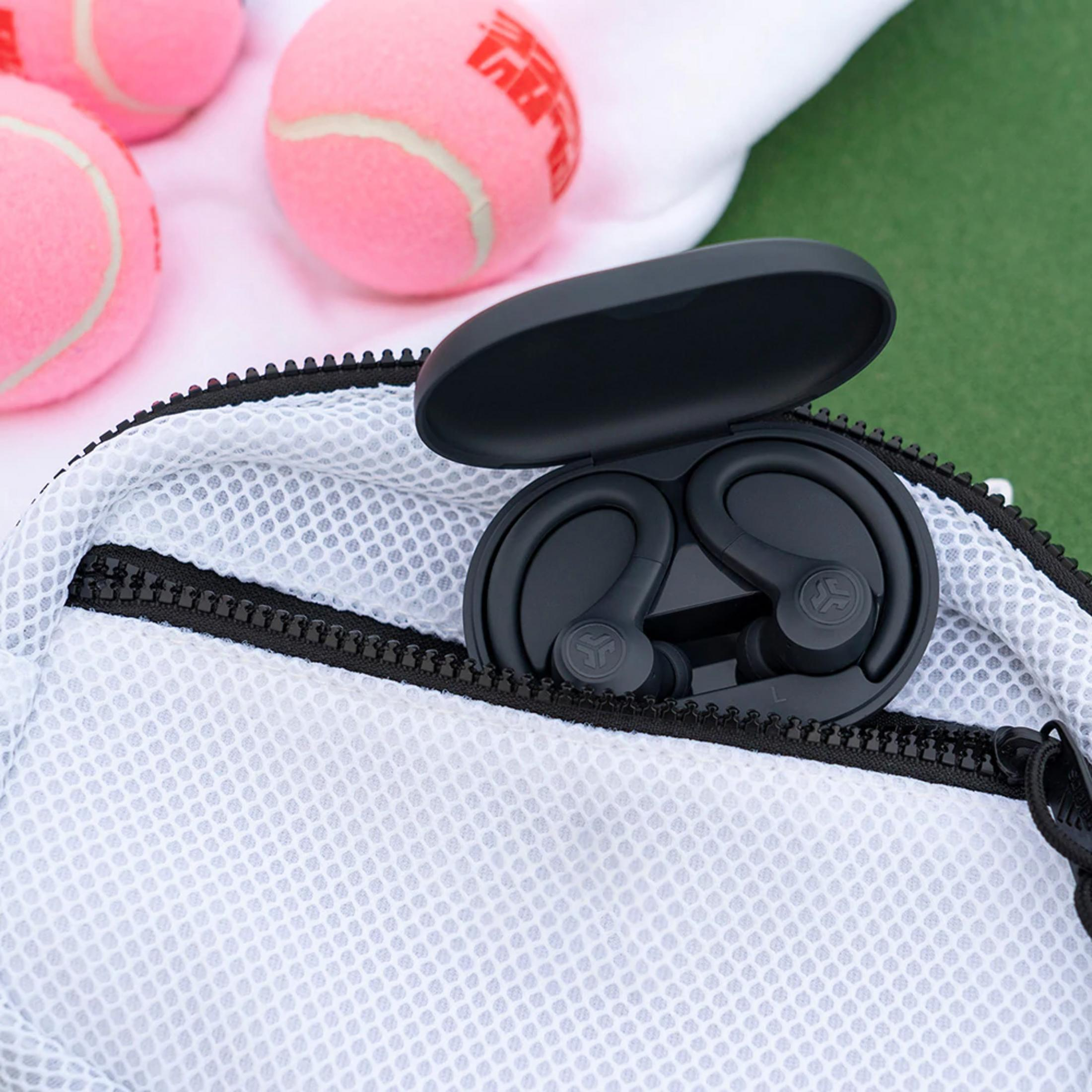 Auricolari neri in custodia di ricarica, dentro una borsa di rete bianca, con palline da tennis rosa.