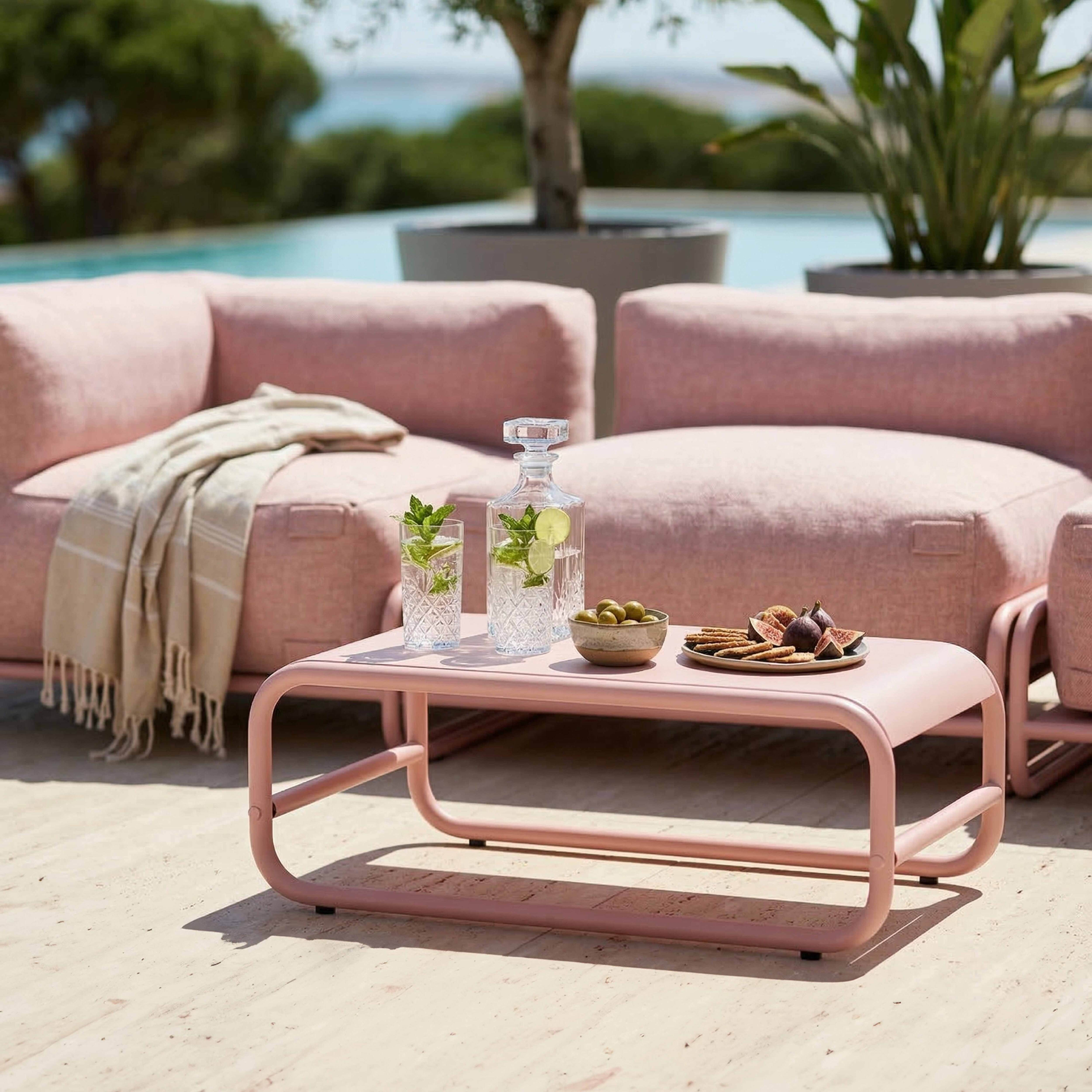 Rosa lounge-möbel am pool mit getränken, snacks und einer decke.