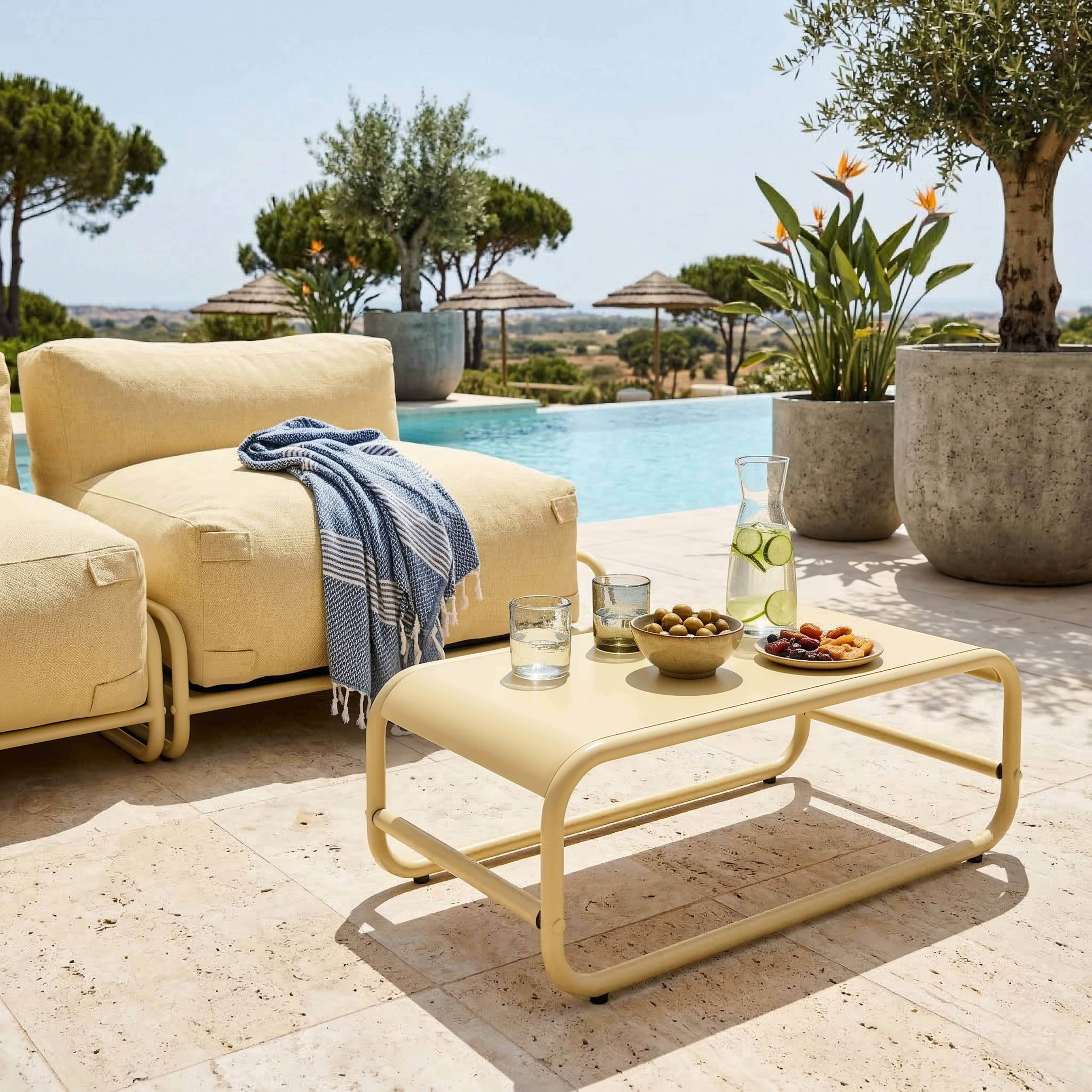 Eine gelbe Couch am Pool mit einer Decke, Getränken und Snacks auf einem Tisch.