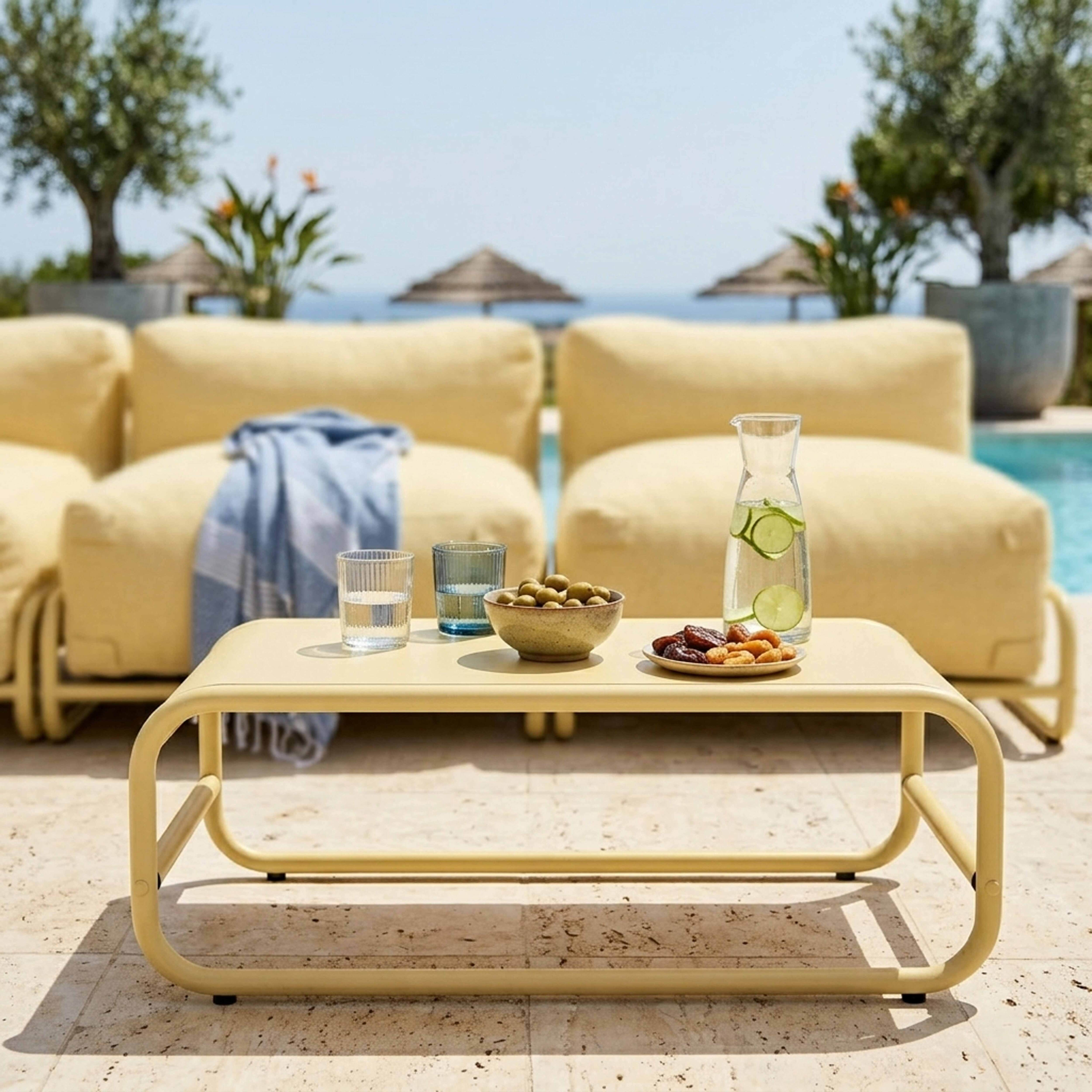 Gelbe Lounge-Möbel am Pool mit einem Tisch, der Getränke und Snacks enthält.