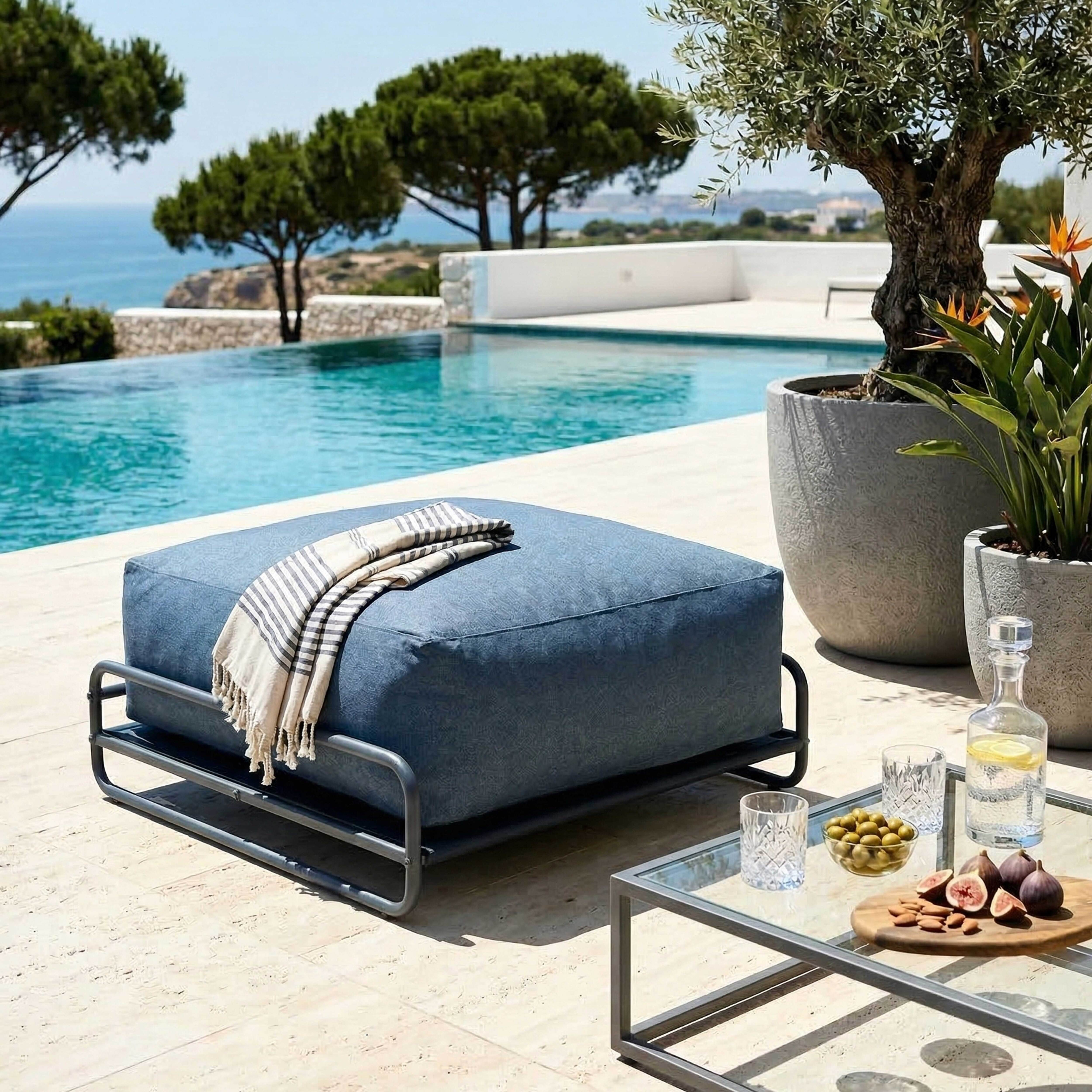 Ein blauer Hocker mit Decke neben einem Pool. Oliven, Feigen und Nüsse auf dem Tisch.