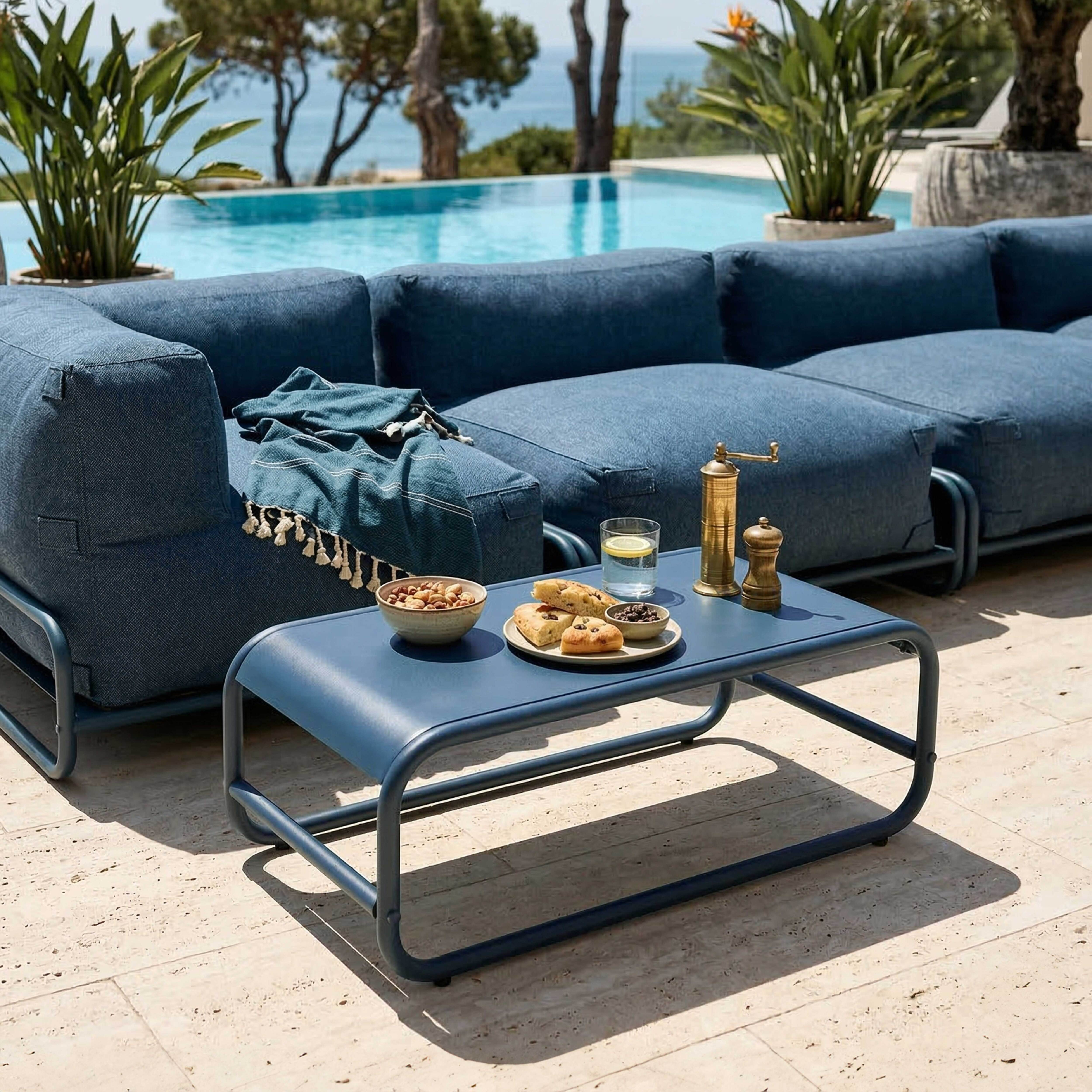 Blaue Outdoor-Möbel am Pool mit Snacks und Getränken am Meer.