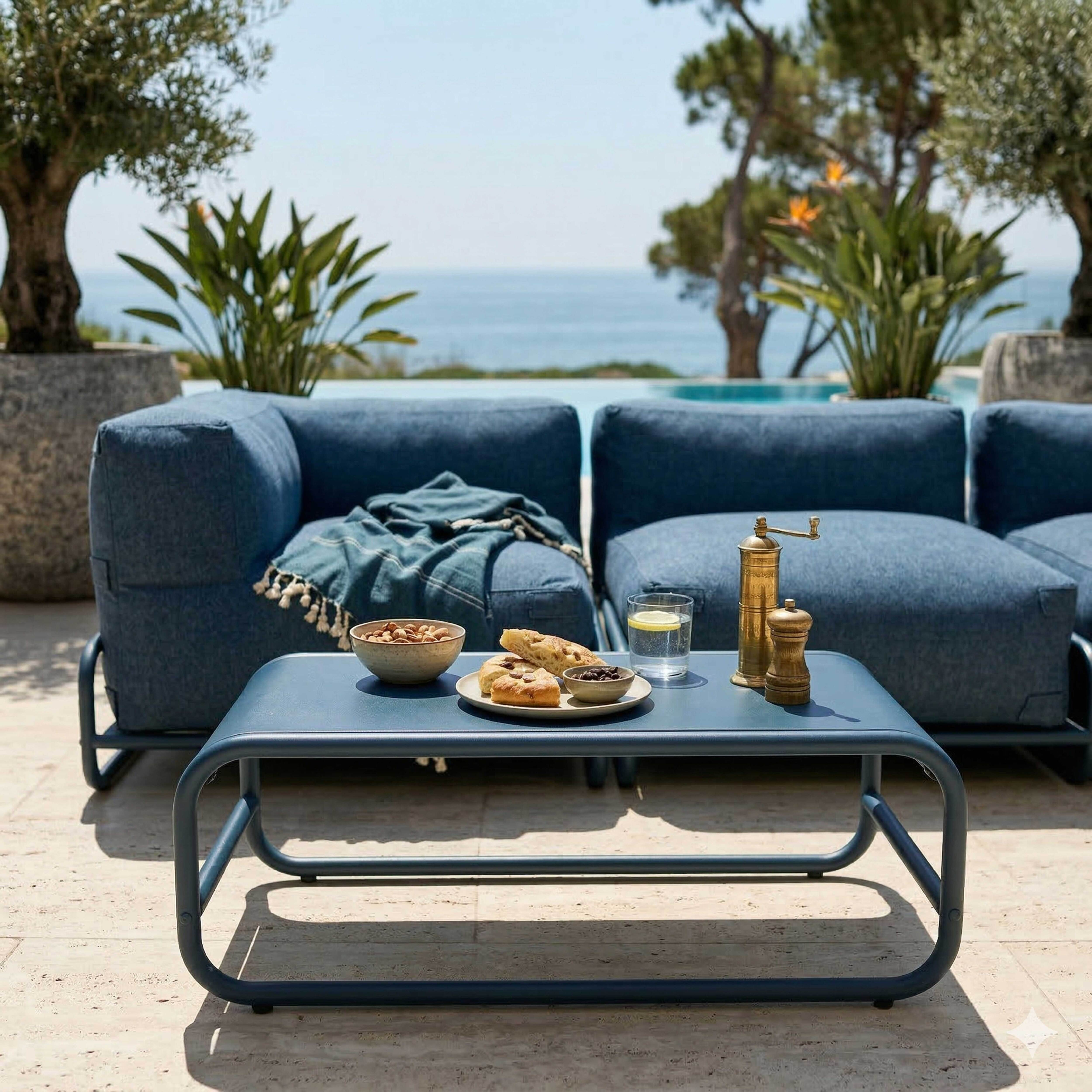 Blaue Loungegarnitur am Pool mit Tisch und Snacks, Meer im Hintergrund.