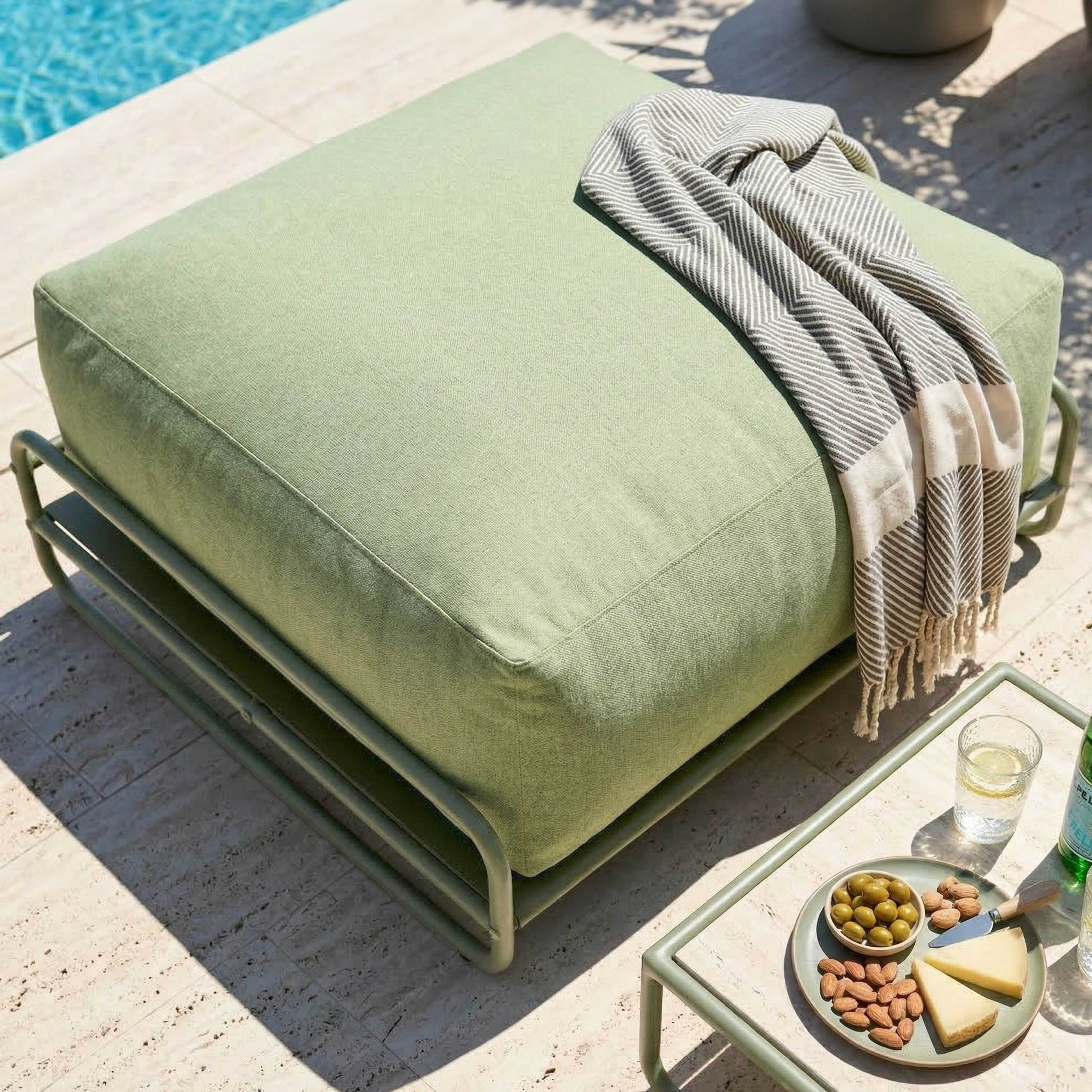 Ein hellgrünes Outdoor-Sitzkissen mit gestreifter Decke neben einem Beistelltisch mit Snacks.