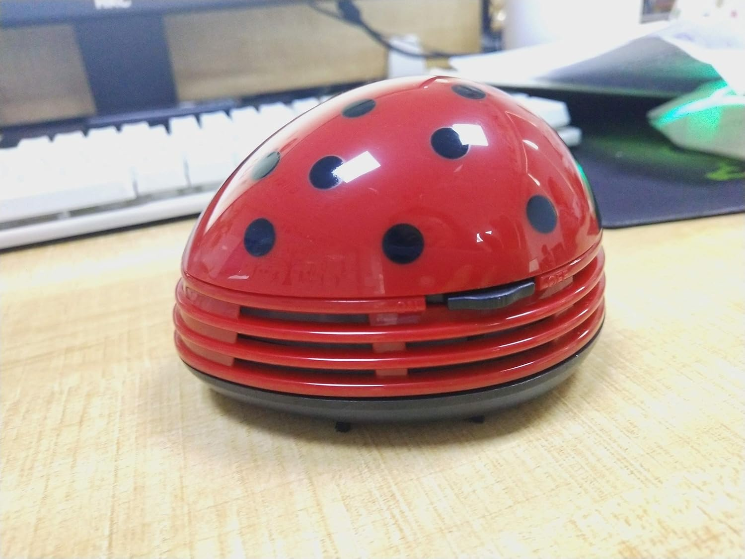 Ein roter Marienkäfer-Mini-Staubsauger mit schwarzen Punkten steht auf einem Holztisch.