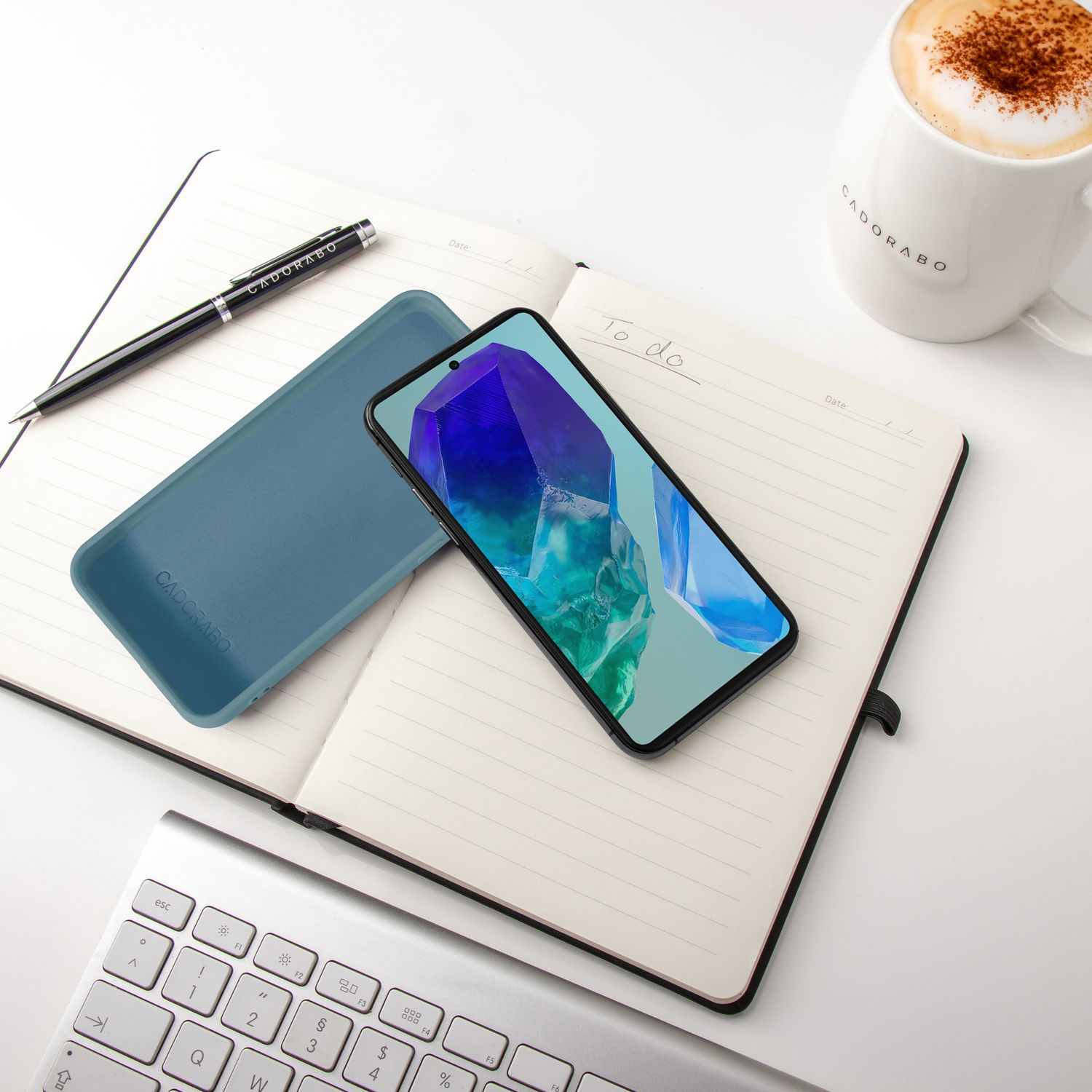 Ein Smartphone auf einem Notizbuch neben einer Tasse Kaffee und einer Tastatur.