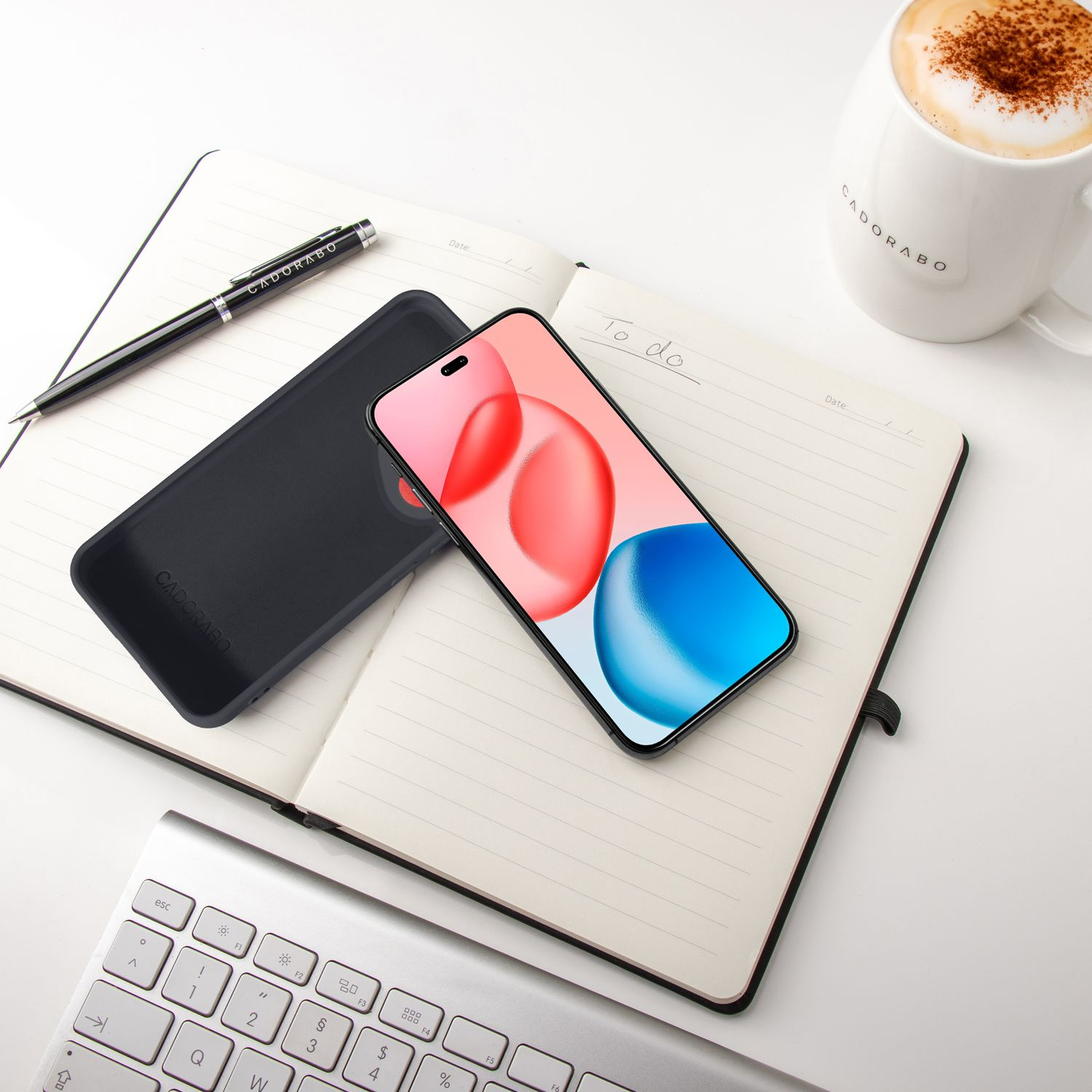 Eine schwarze Handyhülle und ein Smartphone liegen auf einem Notizbuch, neben Stift und Kaffeetasse.
