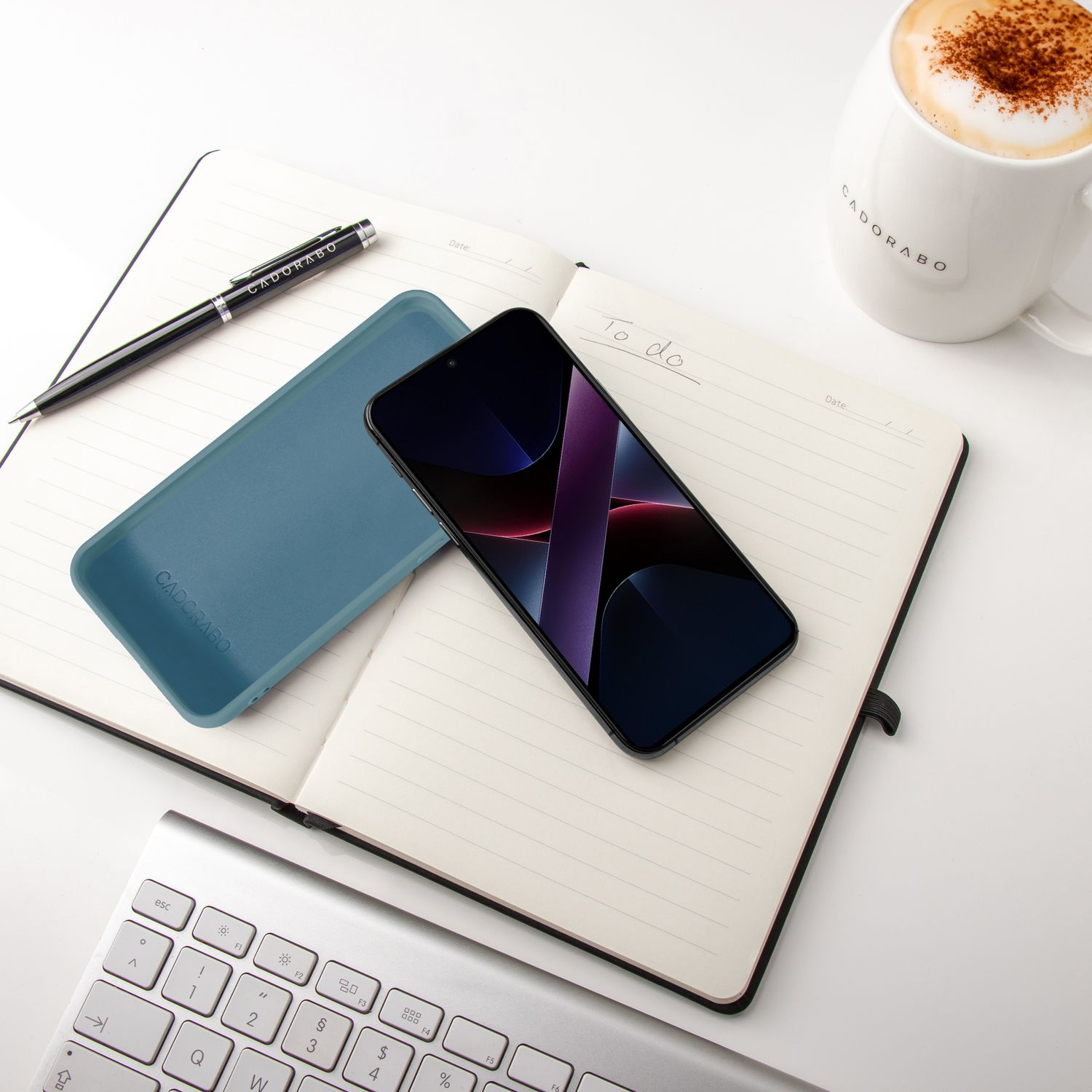 Ein Notizbuch mit Stift, Handy, Hülle und Kaffee auf einem Schreibtisch.