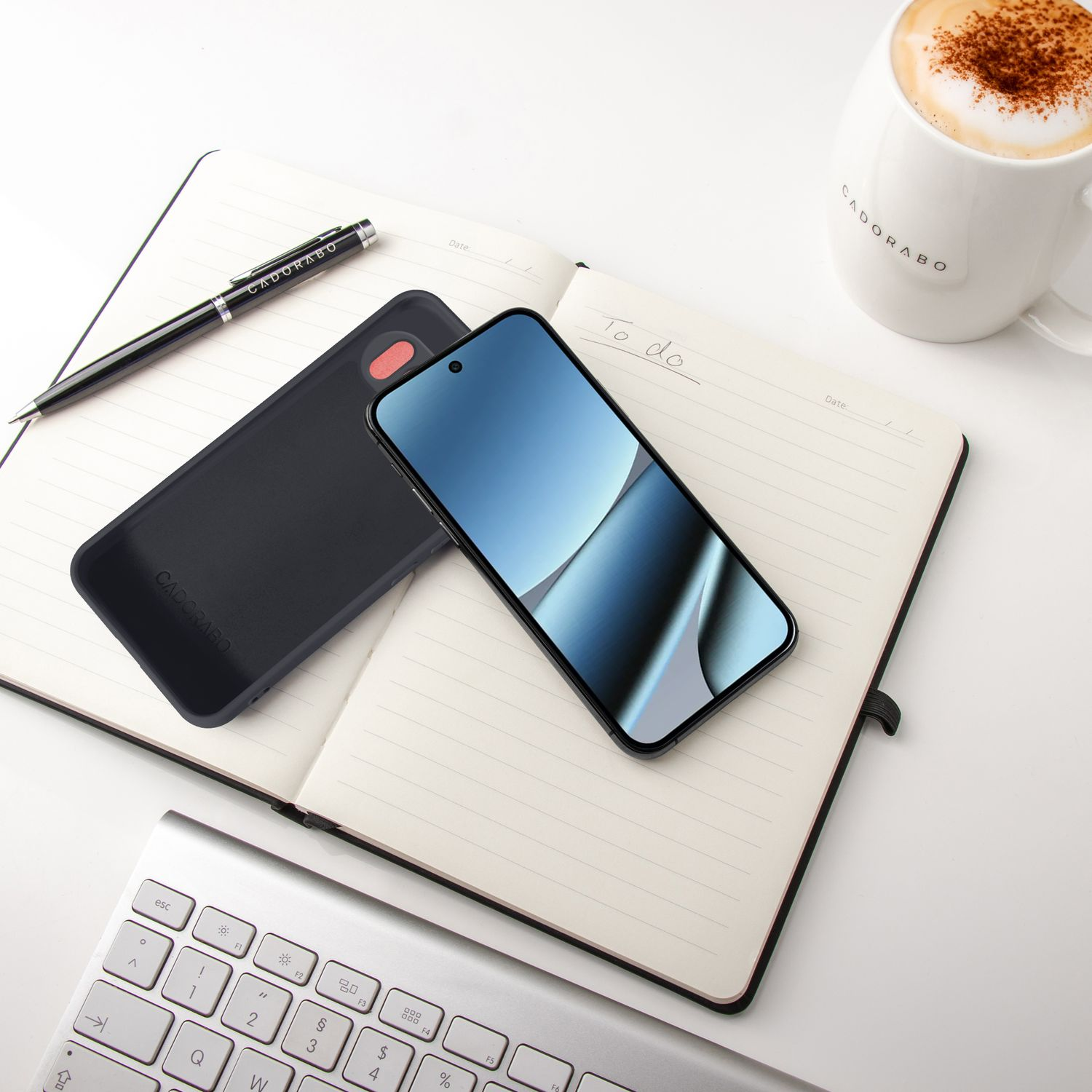Ein schwarzes Smartphone liegt auf einem Notizbuch neben einer Kaffeetasse.