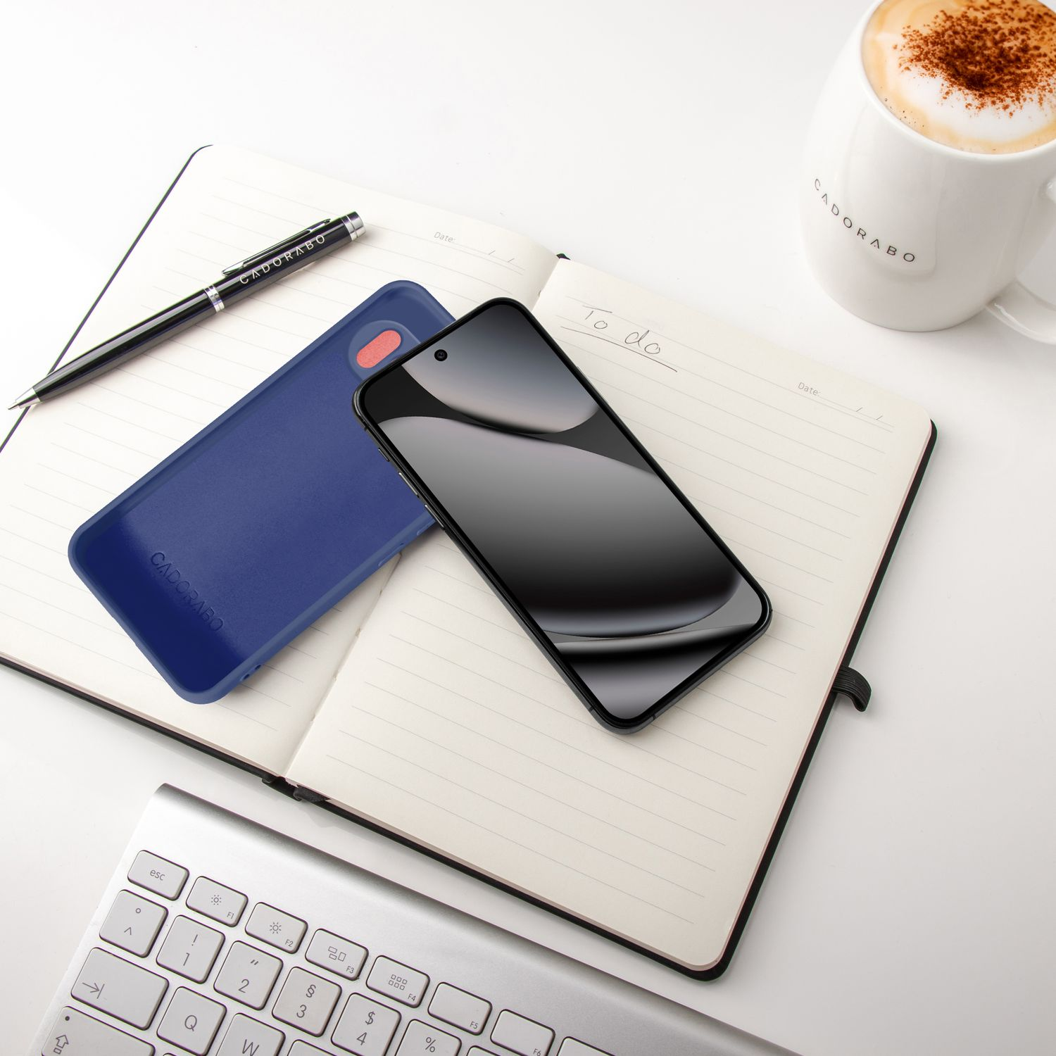Ein Smartphone, eine Handyhülle, ein Notizbuch, ein Stift und eine Kaffeetasse.