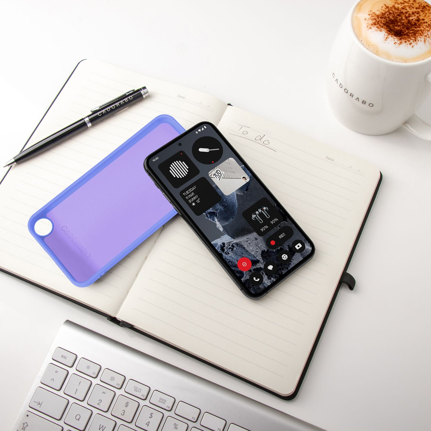 Ein Telefon, eine lila Hülle, ein Notizbuch, ein Stift, eine Tastatur und Kaffee.