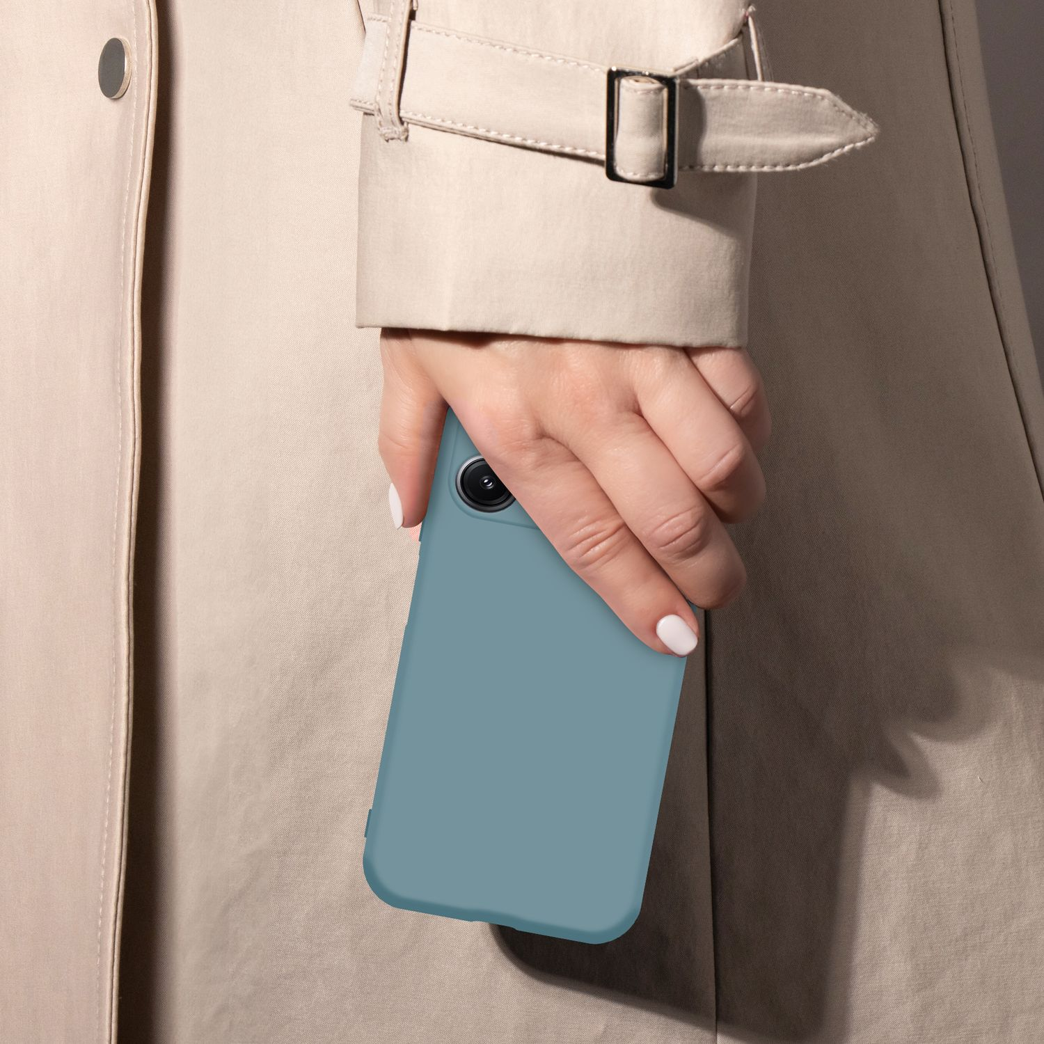 Eine Hand mit weißen Nägeln hält eine blaue Handyhülle gegen einen beigen Trenchcoat.