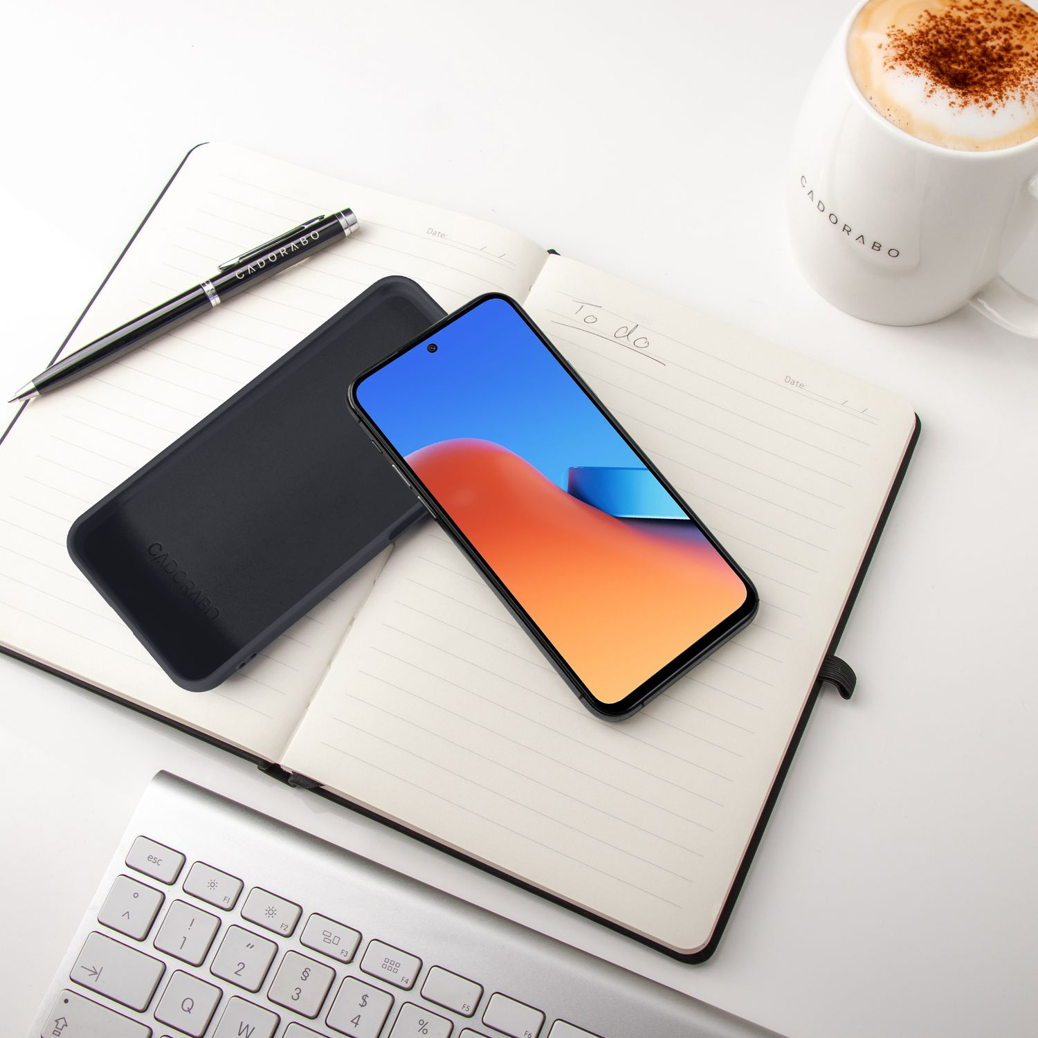 Ein offenes Notizbuch mit einem Smartphone, Stift, einer Tasse Kaffee und einer Tastatur.