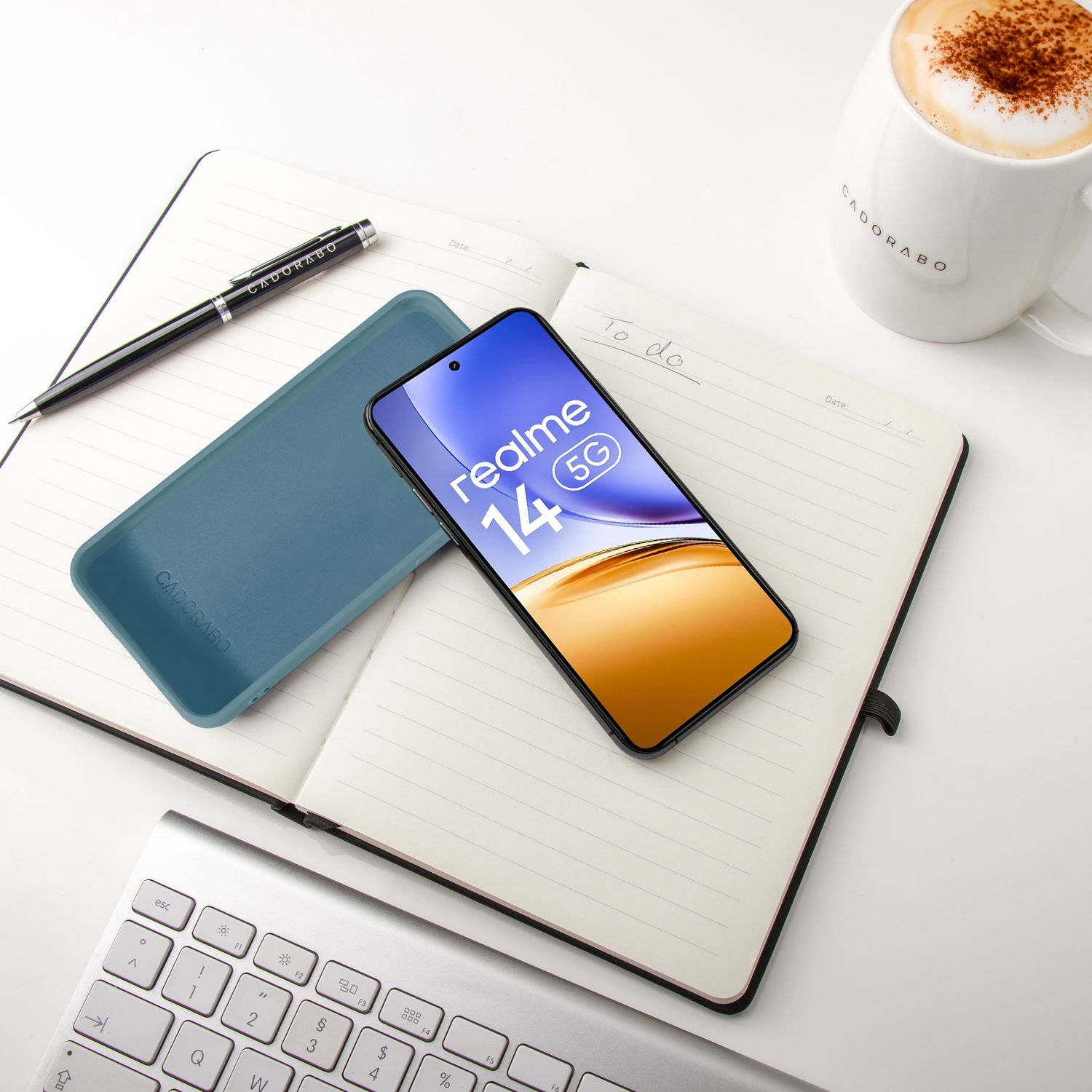 Ein Smartphone liegt auf einem Notizbuch neben einer Kaffeetasse und Tastatur.