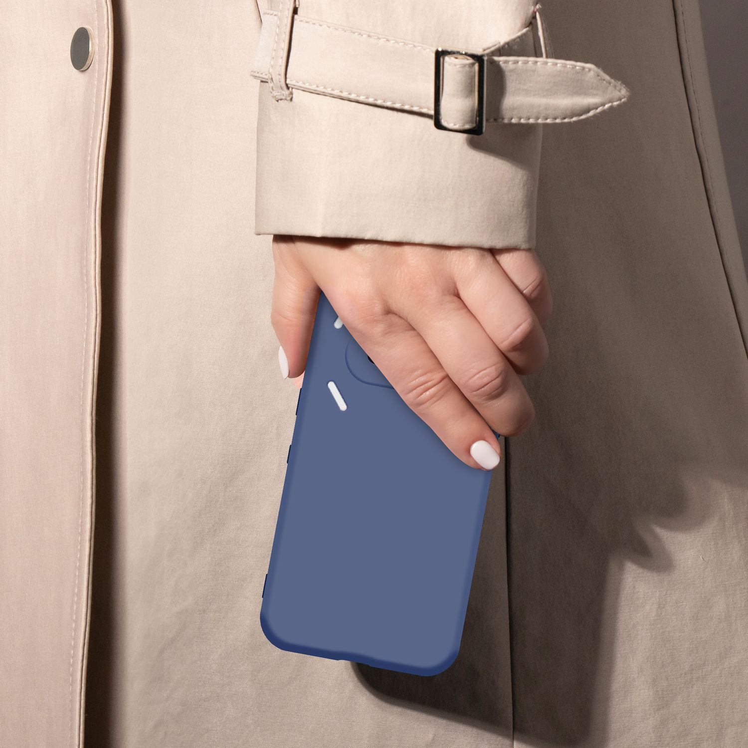 Eine Hand mit weiß lackierten Nägeln hält ein blaues Smartphone vor einem beige Trenchcoat.