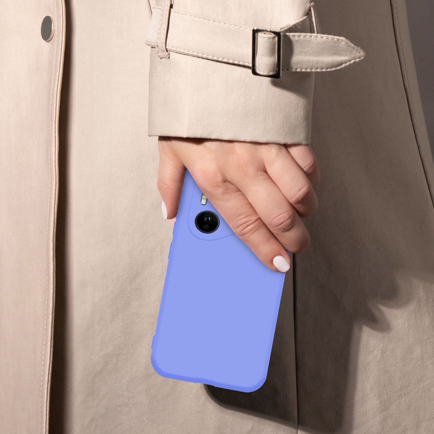 Eine Hand mit weißen Nägeln hält ein hellblaues Smartphone vor einem beigen Trenchcoat.
