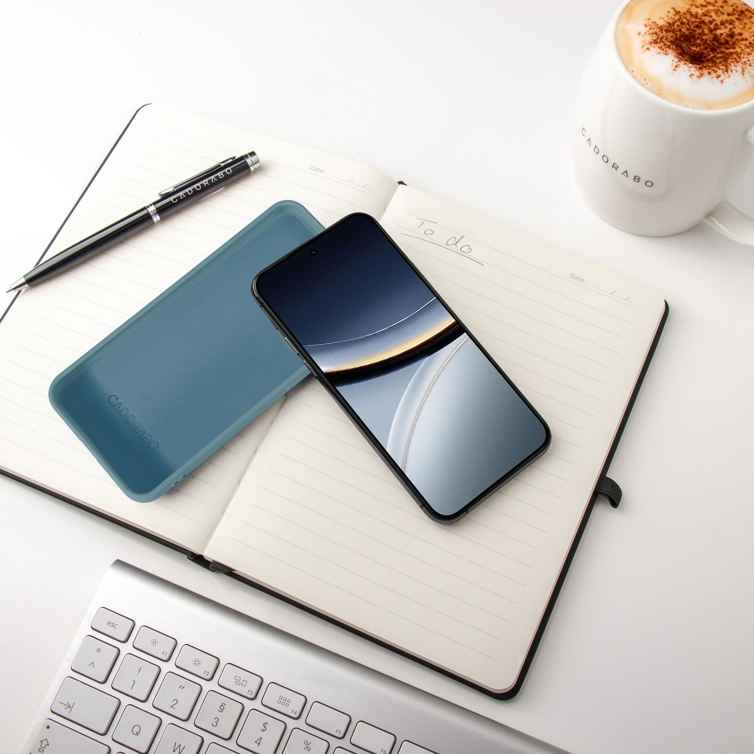 Ein Notizbuch mit Stift, Handy, Hülle, Kaffee und Tastatur.