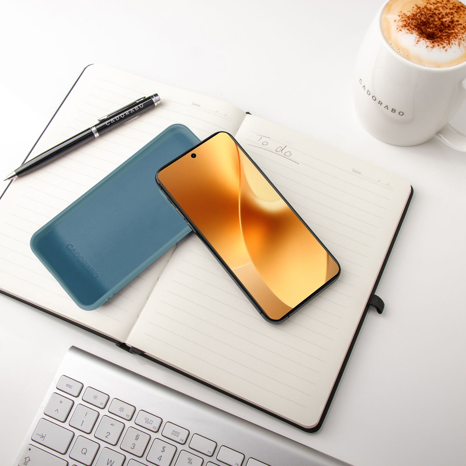 Ein offenes Notizbuch mit Stift, Handyhülle, Smartphone und Kaffeetasse.