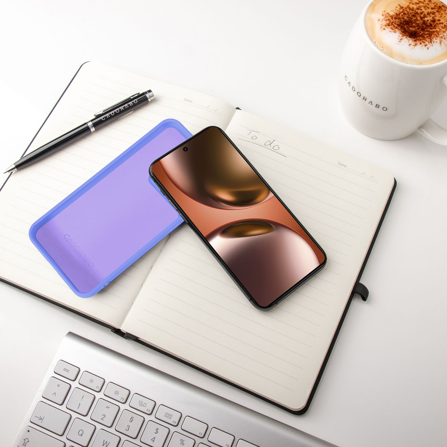 Ein Smartphone liegt auf einem Notizbuch neben einer Kaffeetasse und Tastatur.