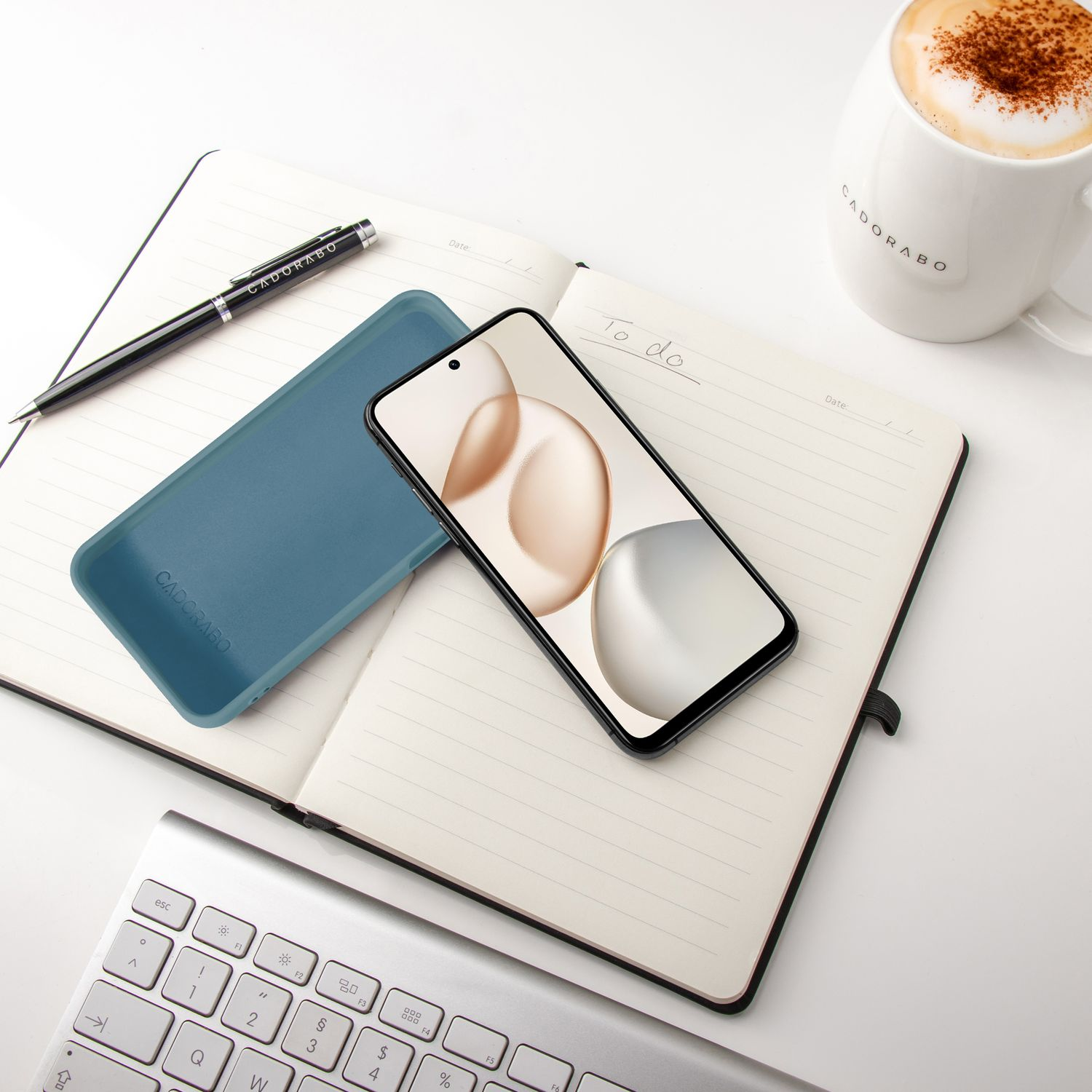 Ein Smartphone, Hülle, Stift und Notizbuch liegen auf einem Schreibtisch.