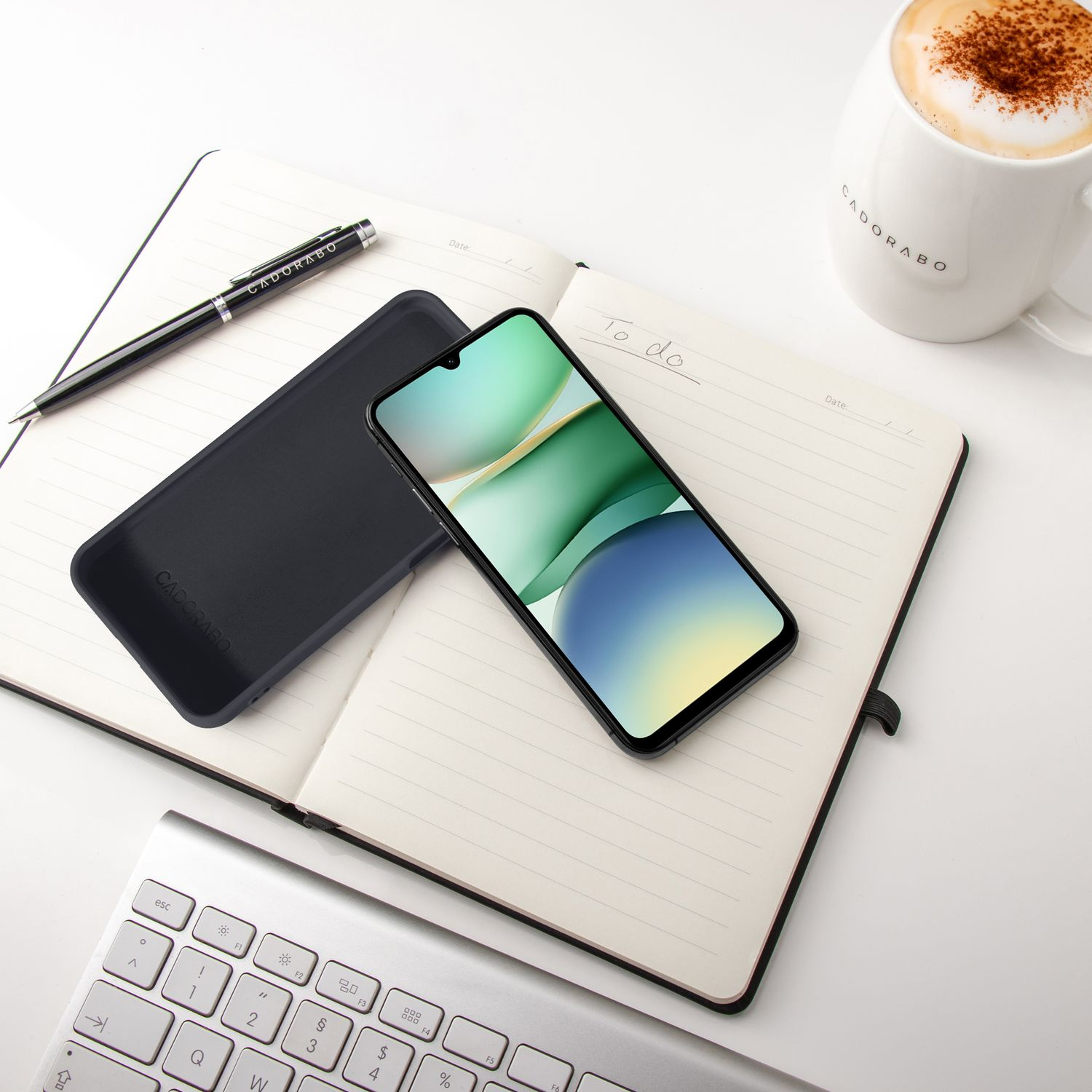 Ein Smartphone liegt auf einem Notizbuch neben einer Tasse Kaffee und einer Tastatur.