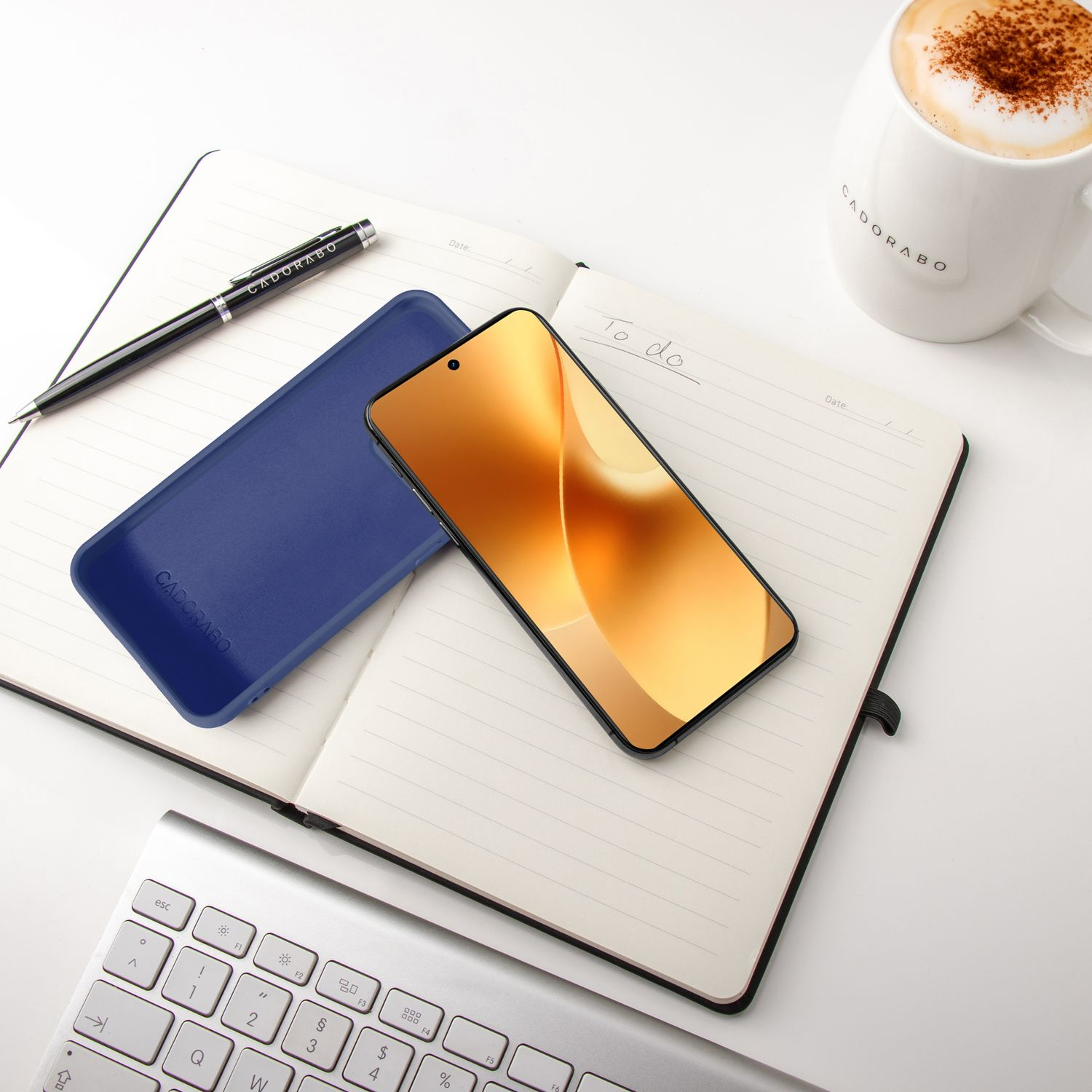 Ein aufgeschlagenes Notizbuch mit Handy, Stift, Tastatur und Kaffee.
