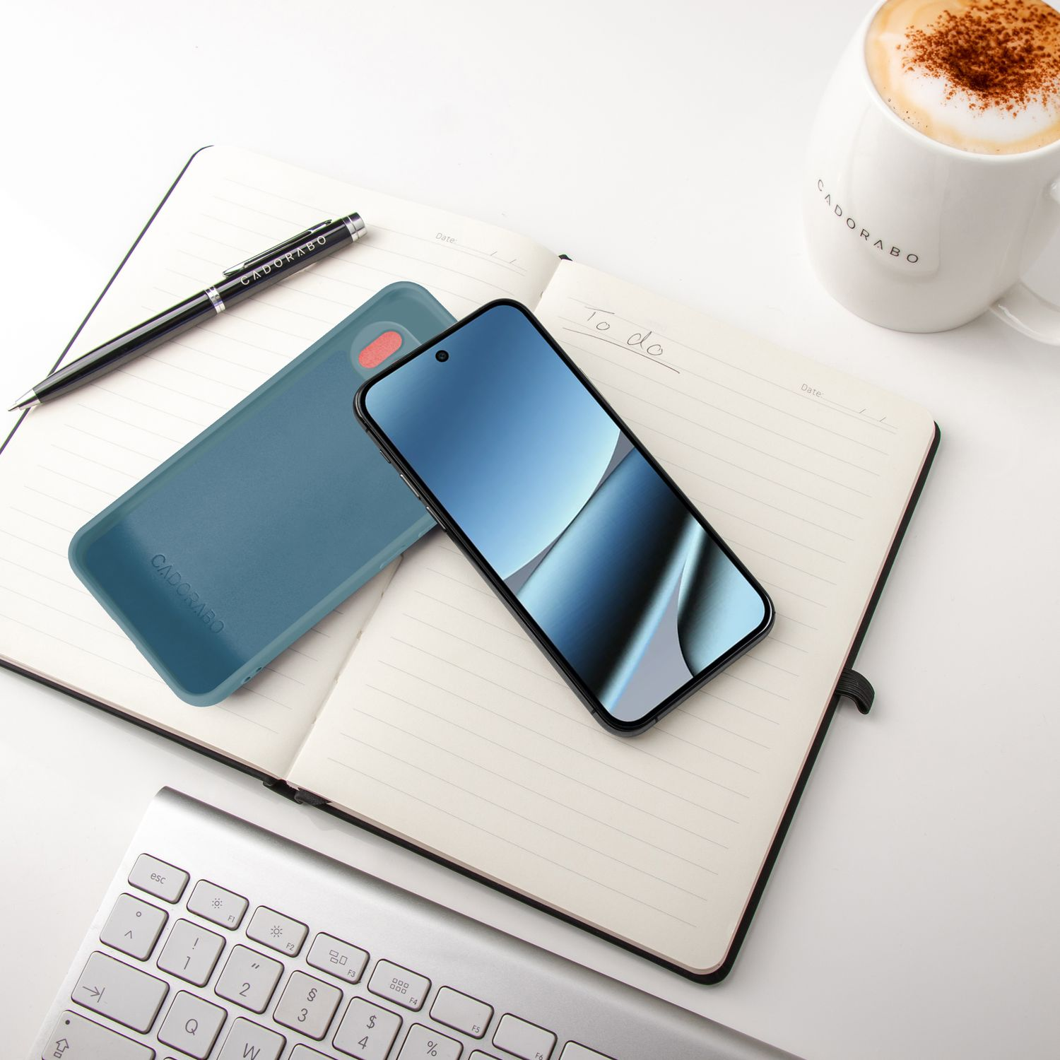 Ein Smartphone, eine Hülle, ein Notizbuch, ein Stift und eine Kaffeetasse auf einem Schreibtisch.