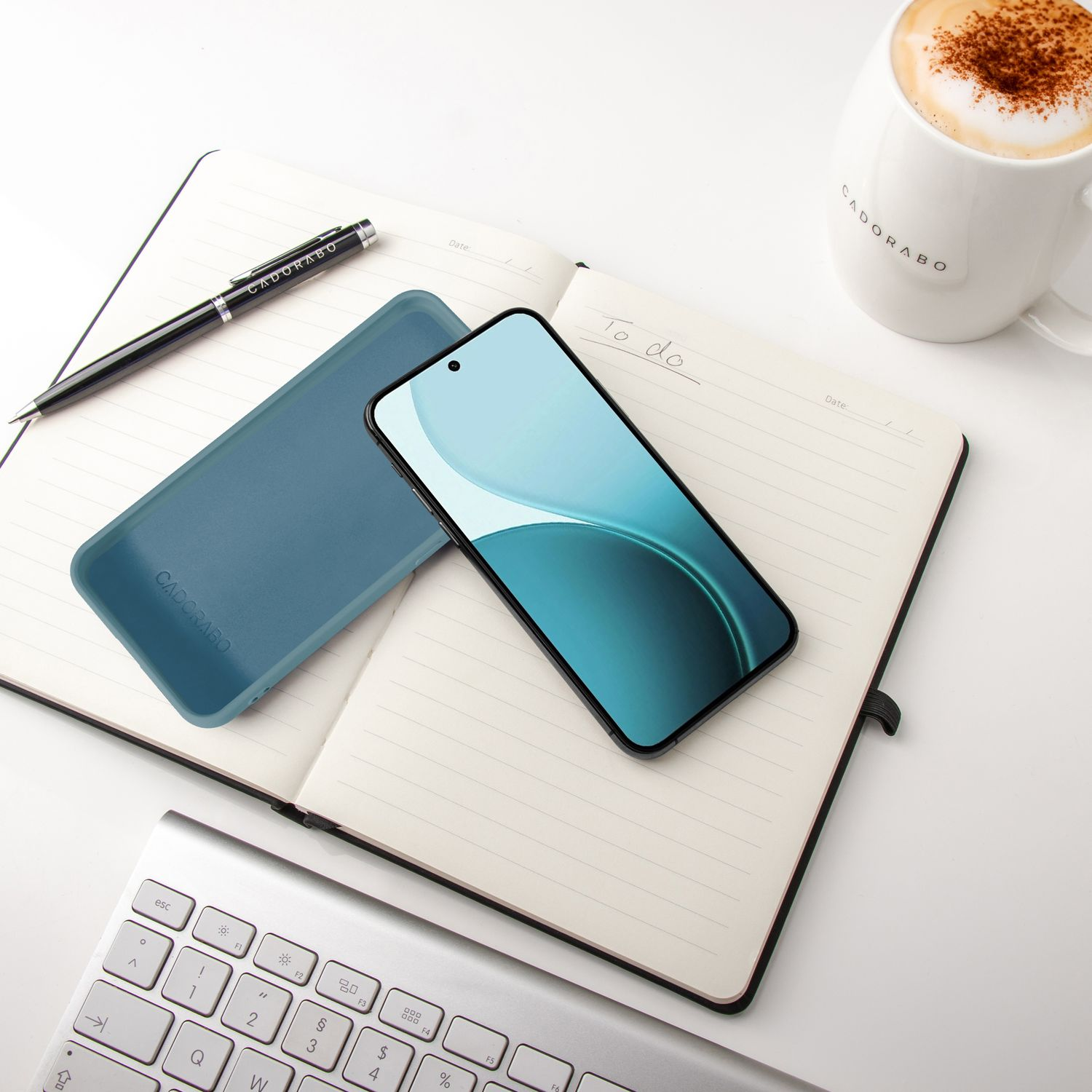 Ein aufgeschlagenes Notizbuch mit Handy, Stift, Kaffee und Tastatur.