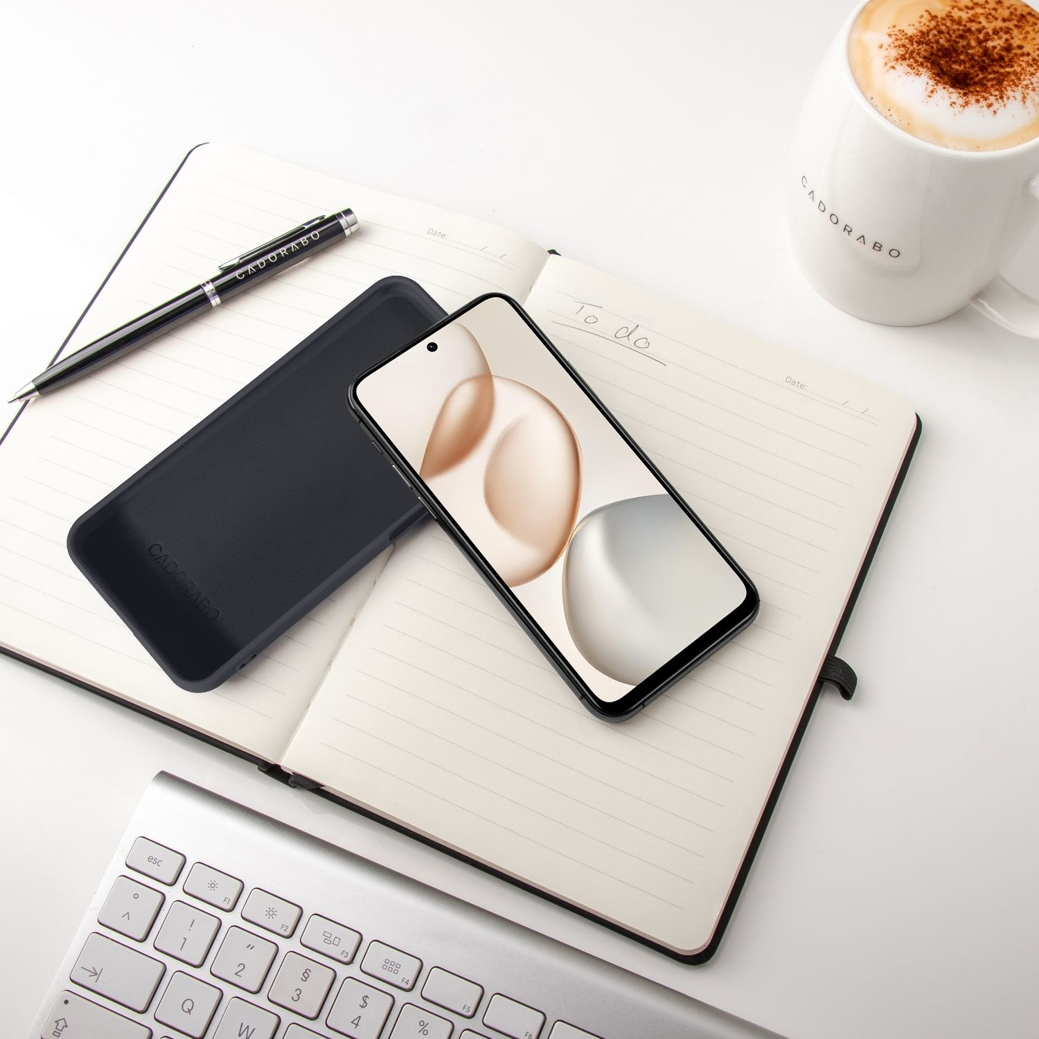 Ein aufgeschlagenes Notizbuch mit einem Handy, Stift, Tastatur und Kaffee.