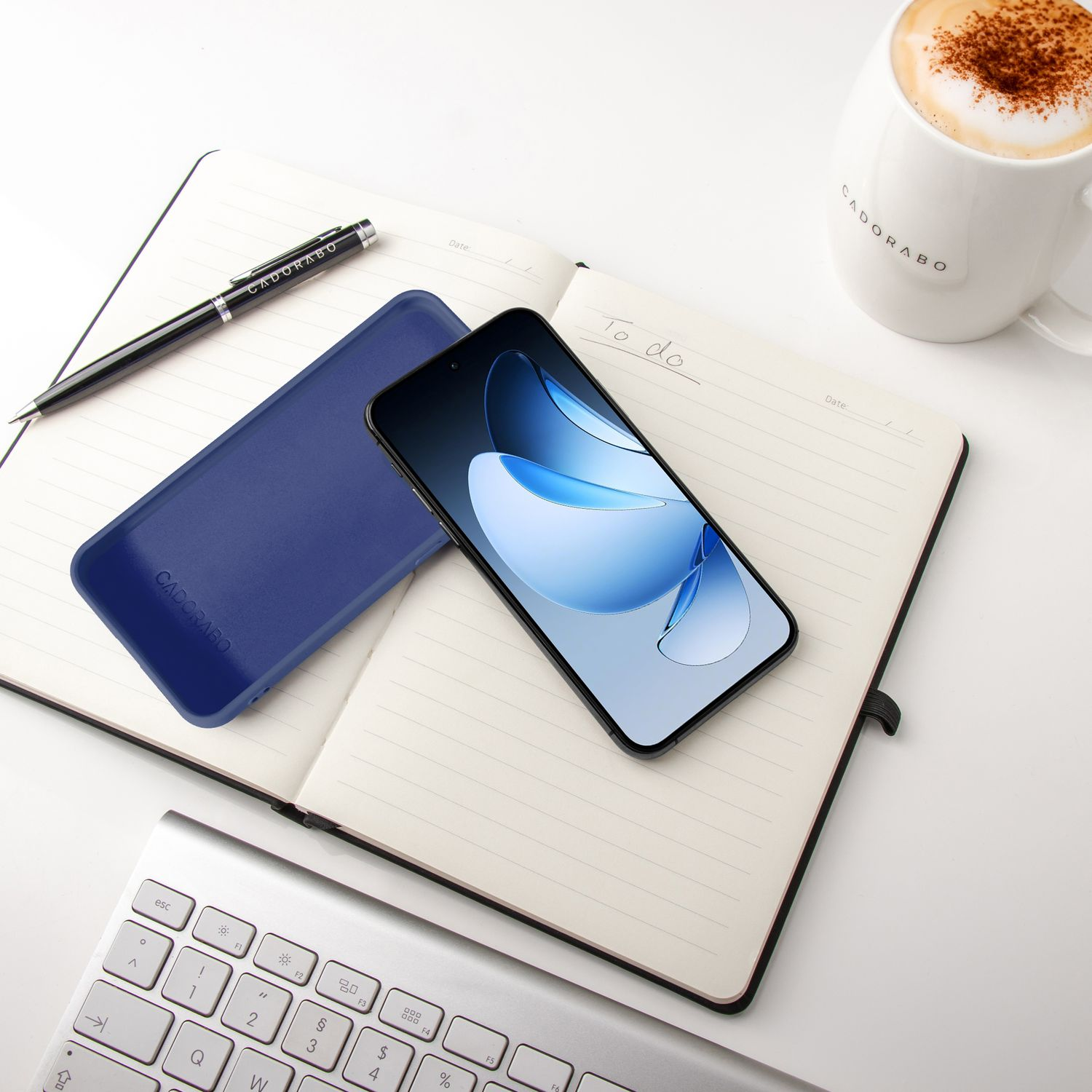 Ein Smartphone, Notizbuch, Stift, eine Tasse Kaffee und eine Tastatur auf weißem Tisch.