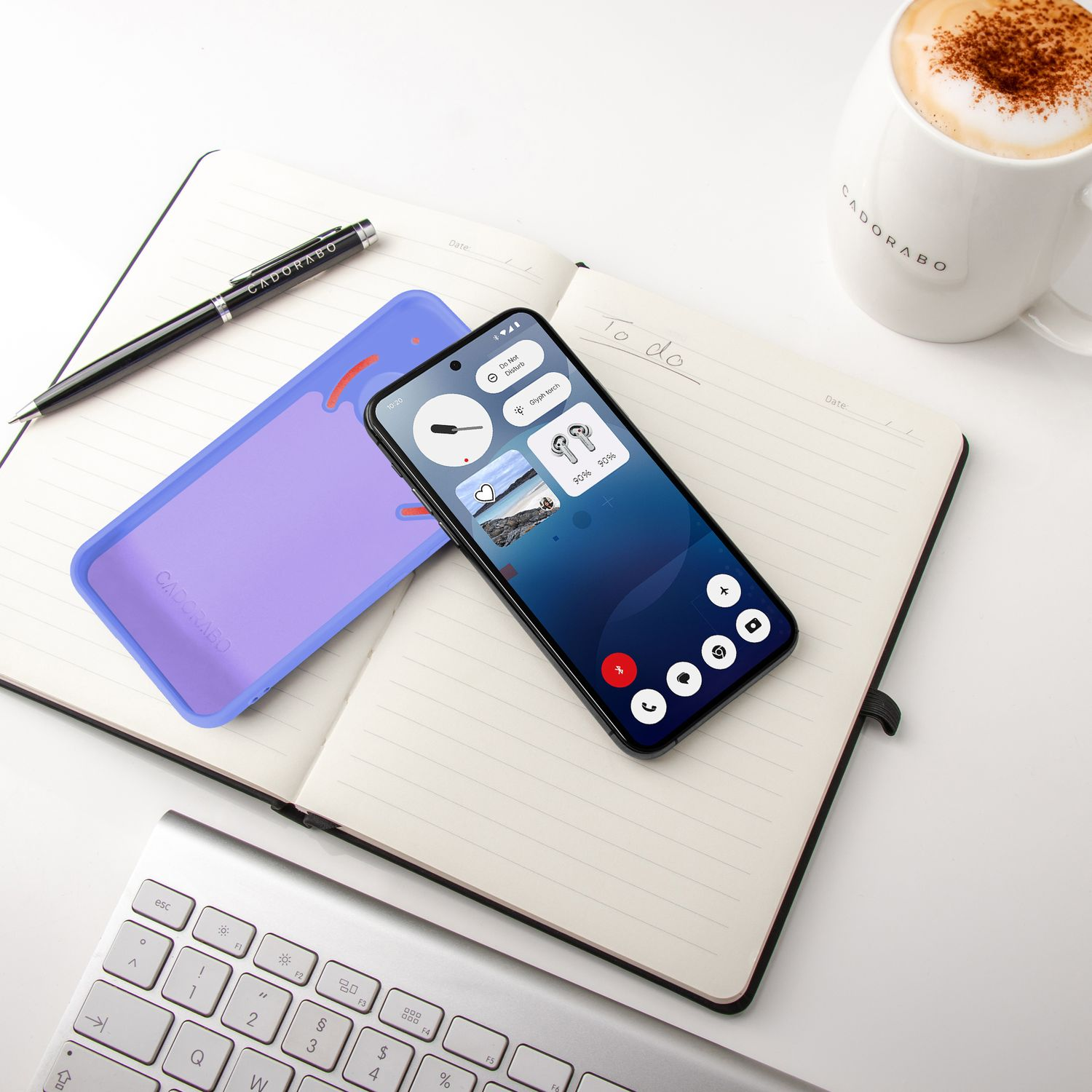 Ein Smartphone liegt auf einem Notizbuch neben einer Kaffeetasse und Tastatur.