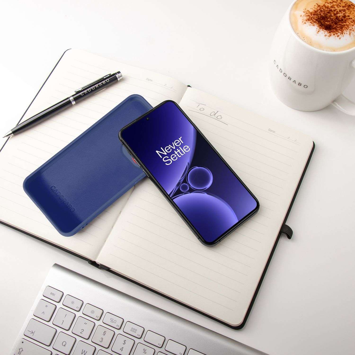 Ein Smartphone, eine Hülle, ein Notizbuch, ein Stift, eine Tasse Kaffee und eine Tastatur.