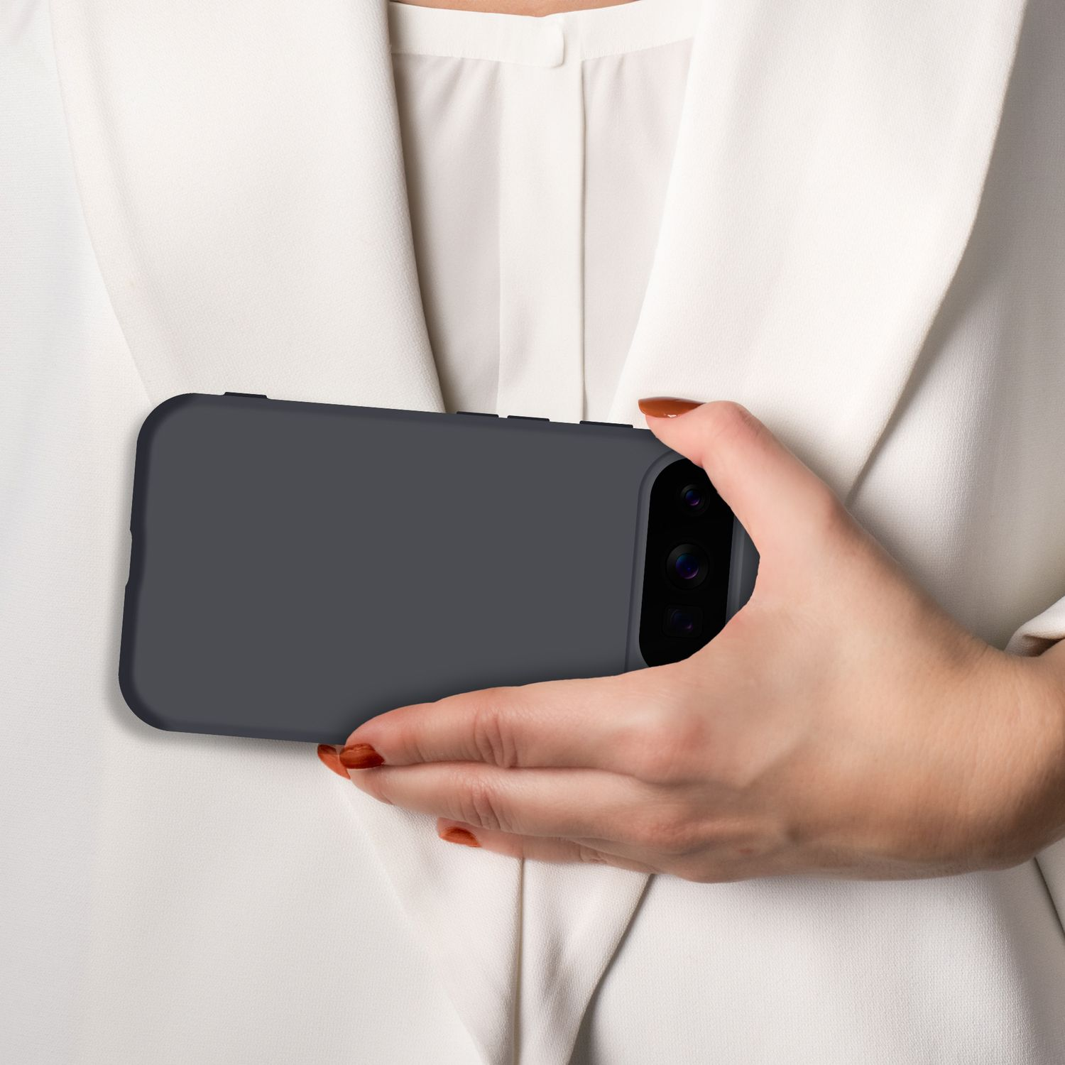 Eine Hand mit braun lackierten Nägeln hält ein dunkles Smartphone vor einem weißen Hemd.