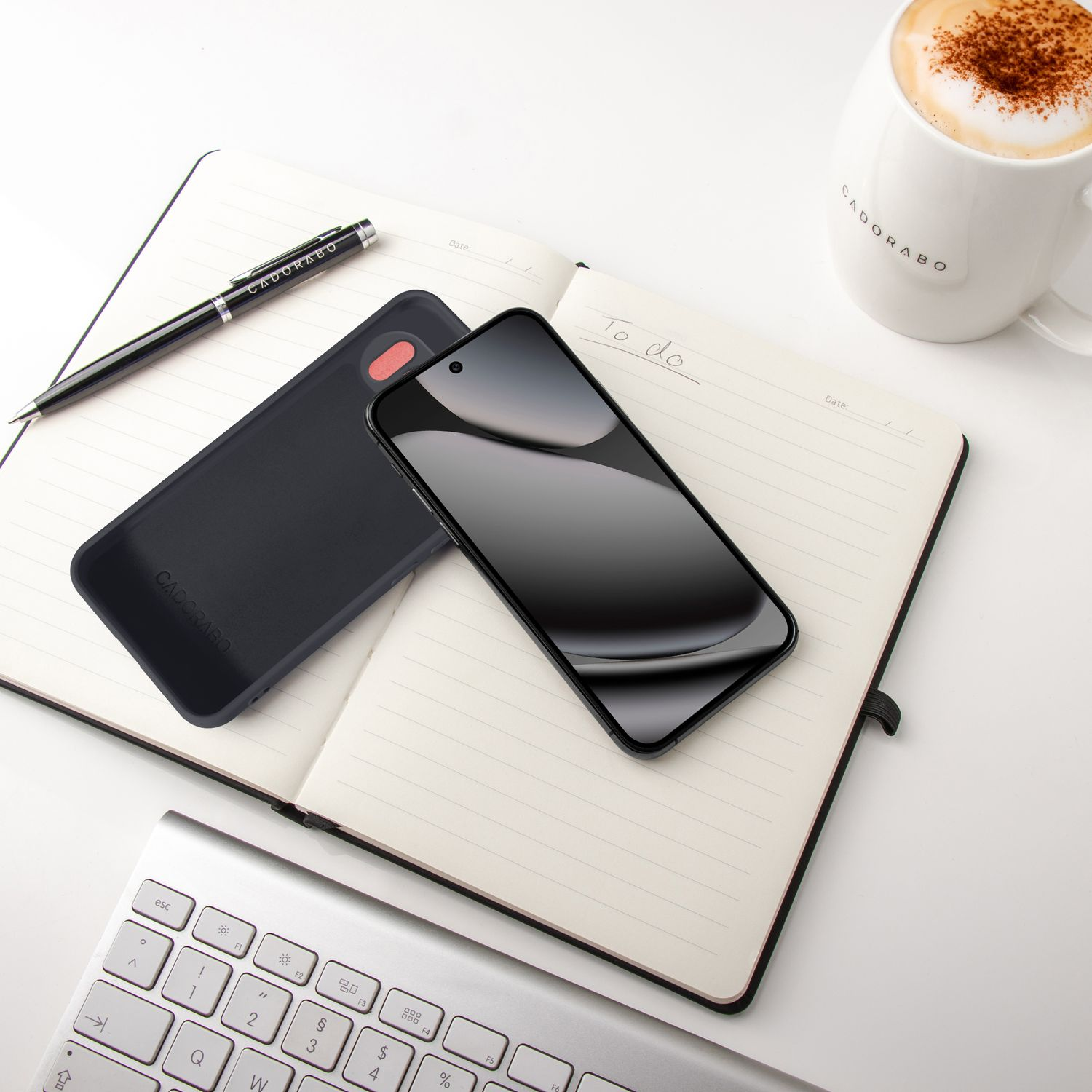 Ein Notizbuch mit Stift, Handyhülle, Smartphone und einer Kaffeetasse.